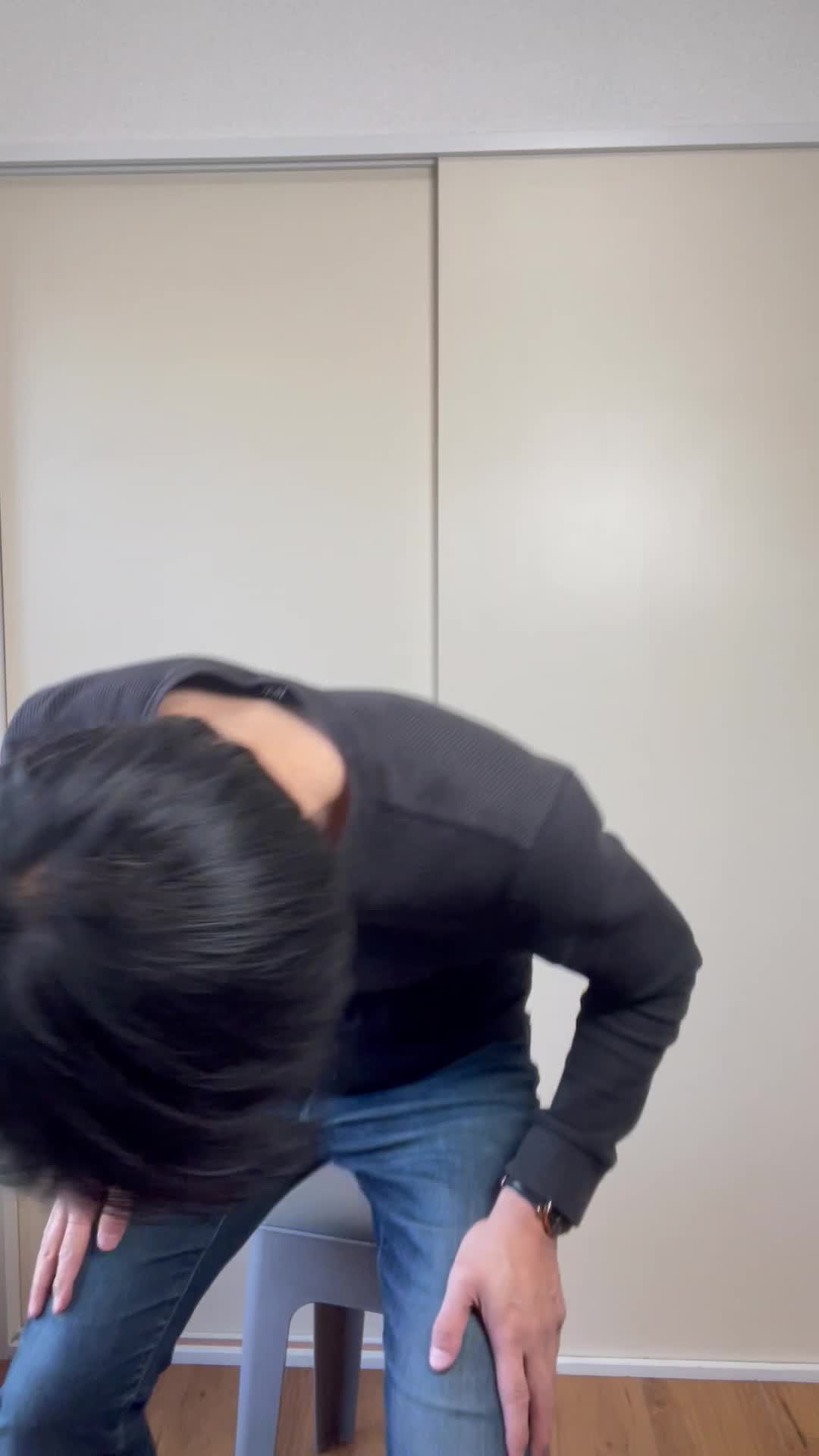 椅子に浅く腰掛け、「下腹部を両手で押さえて痛みを和らげようとする」動作