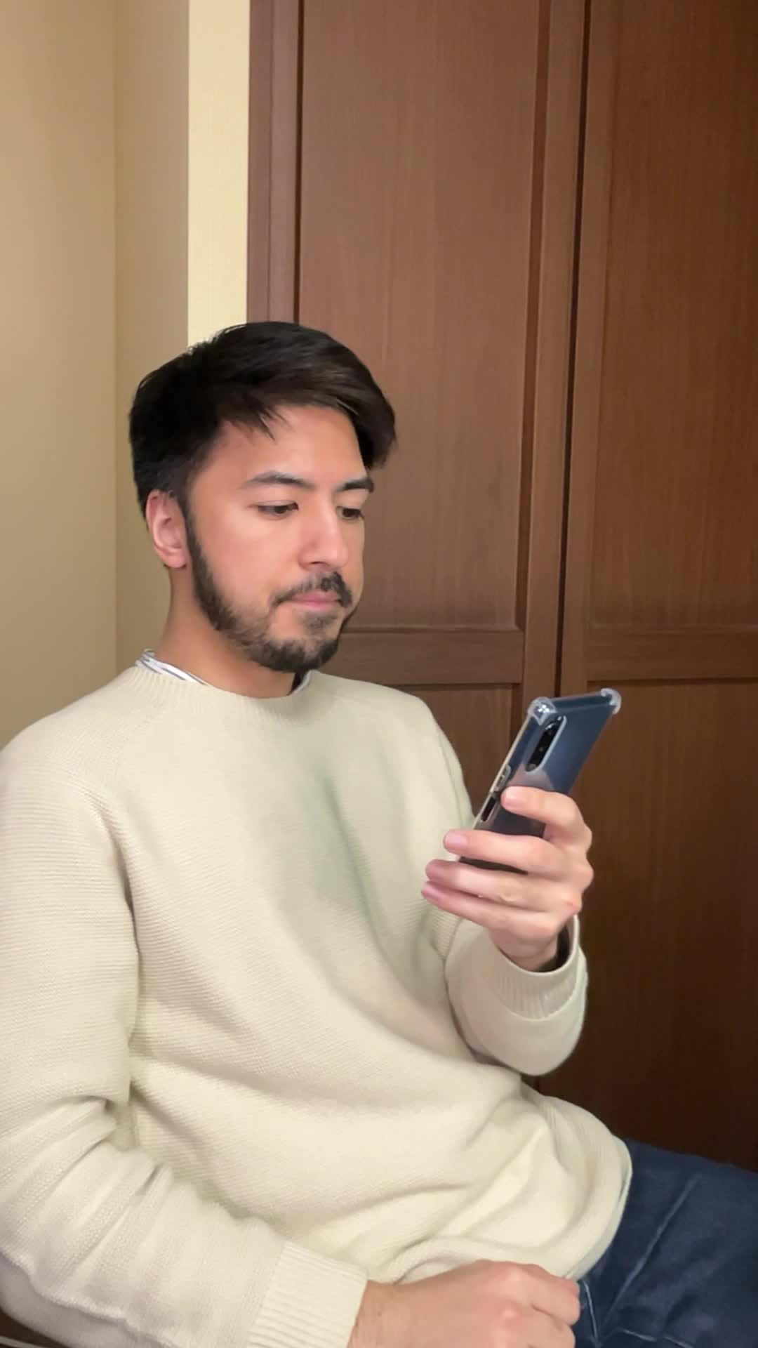 椅子に腰掛け、スマホの画面を見て「白髪ケアの口コミを読んで納得する」表情