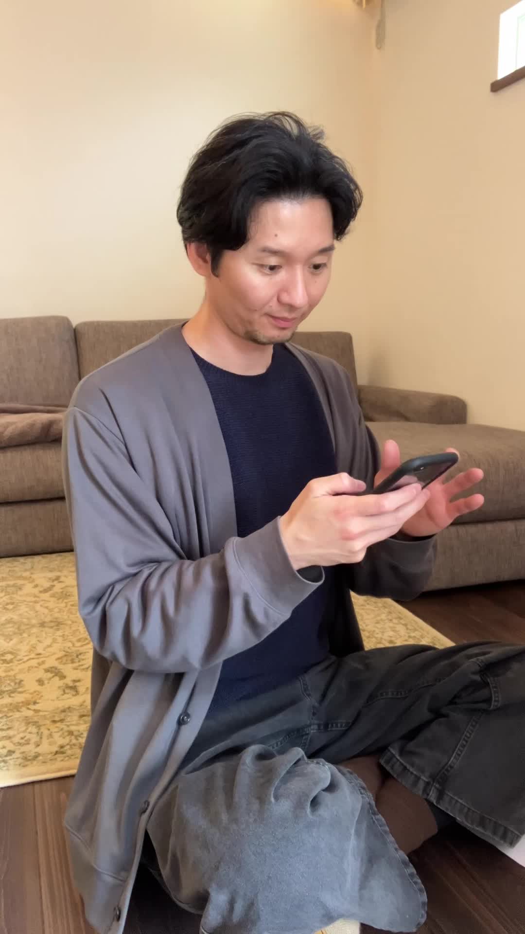 床に座り込み、スマホで「保険の口コミ」を見ながら少し安心した表情を浮かべる