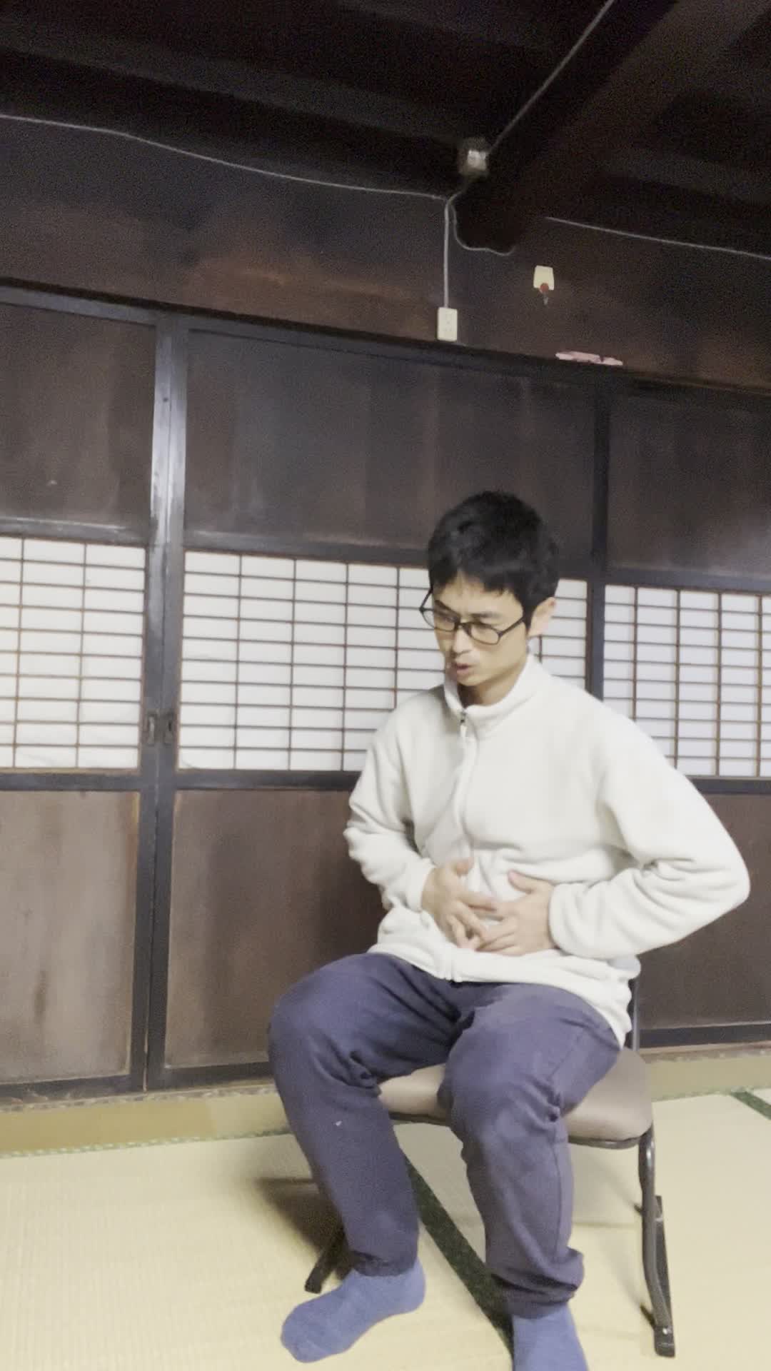 椅子に浅く腰掛け、「下腹部を両手で押さえて痛みを和らげようとする」動作