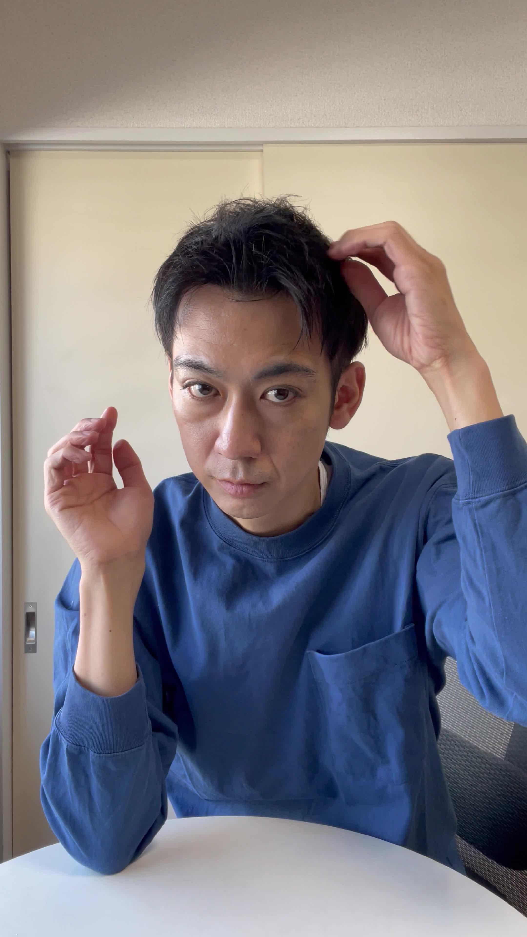 椅子に座り、手でこめかみを押さえながら「最近ずっと頭が重い」と困った表情