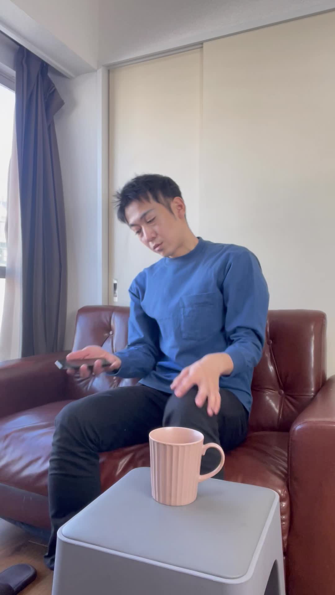 ソファで膝を曲げながら、「疲れた体に何が必要か考えて健康ドリンクを検討する」様子