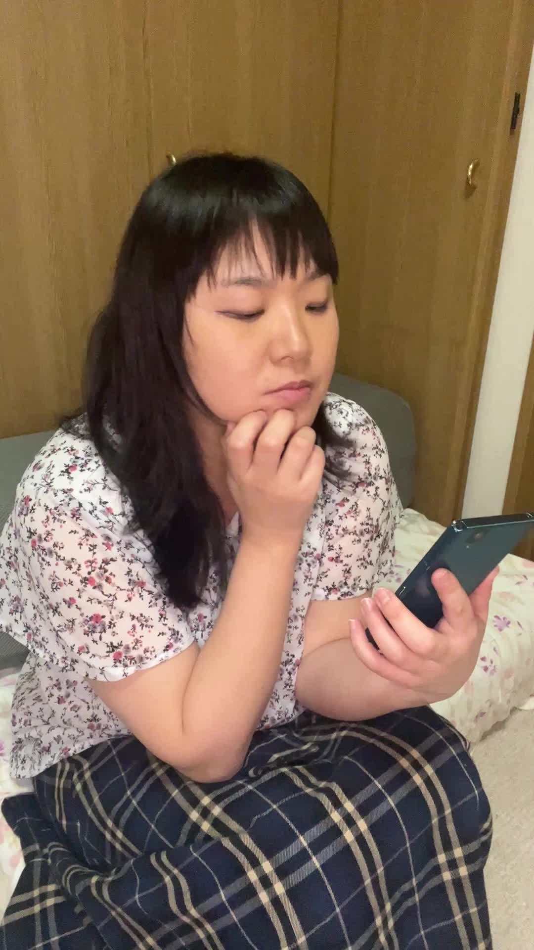 ソファに座り、スマホを見つめながら軽くため息をつき、また微笑む様子