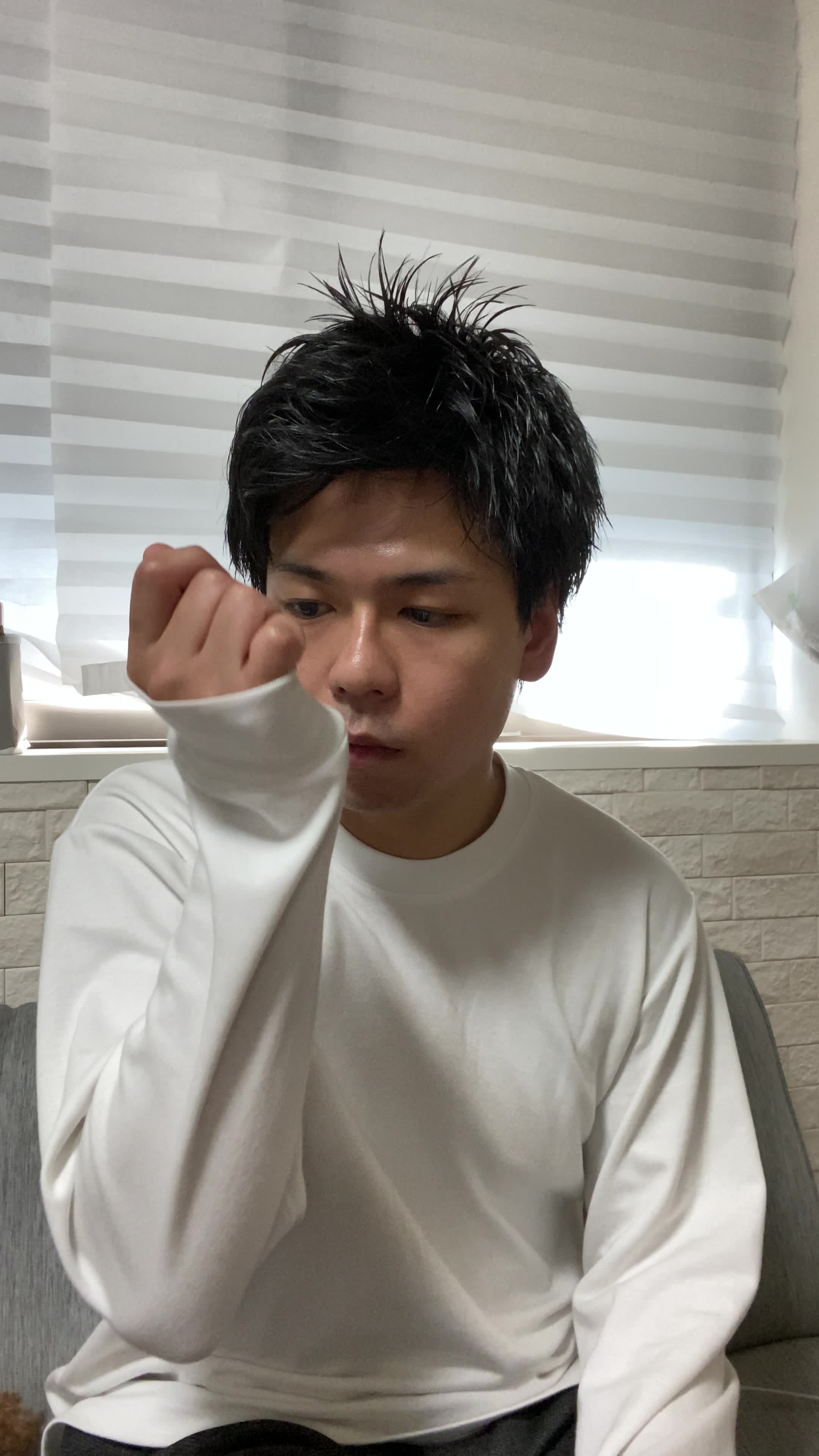 椅子に座り、少し緊張した表情で自分の服の袖を軽く嗅ぐ様子