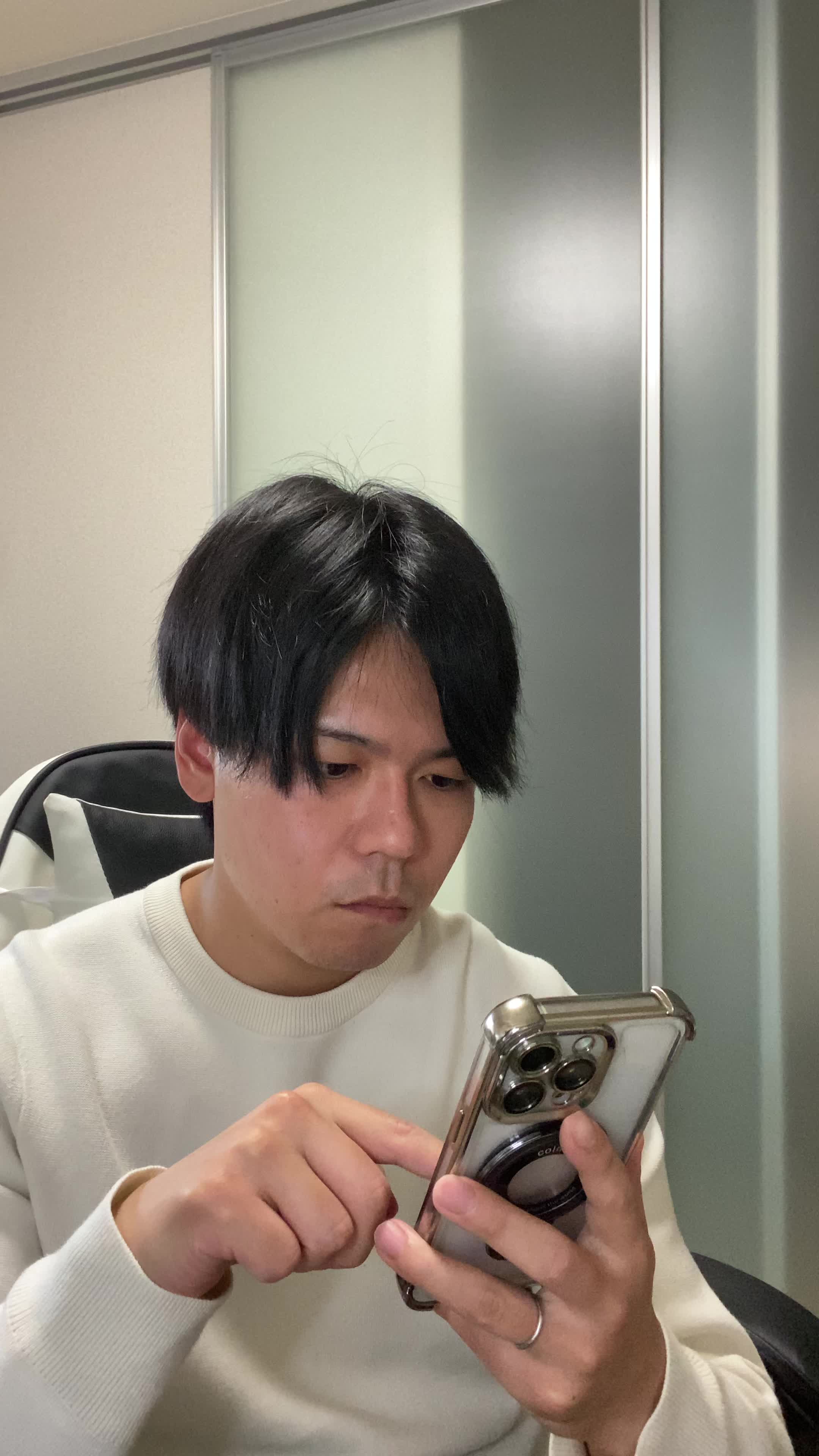 椅子に腰掛け、スマホの画面を見て「白髪ケアの口コミを読んで納得する」表情