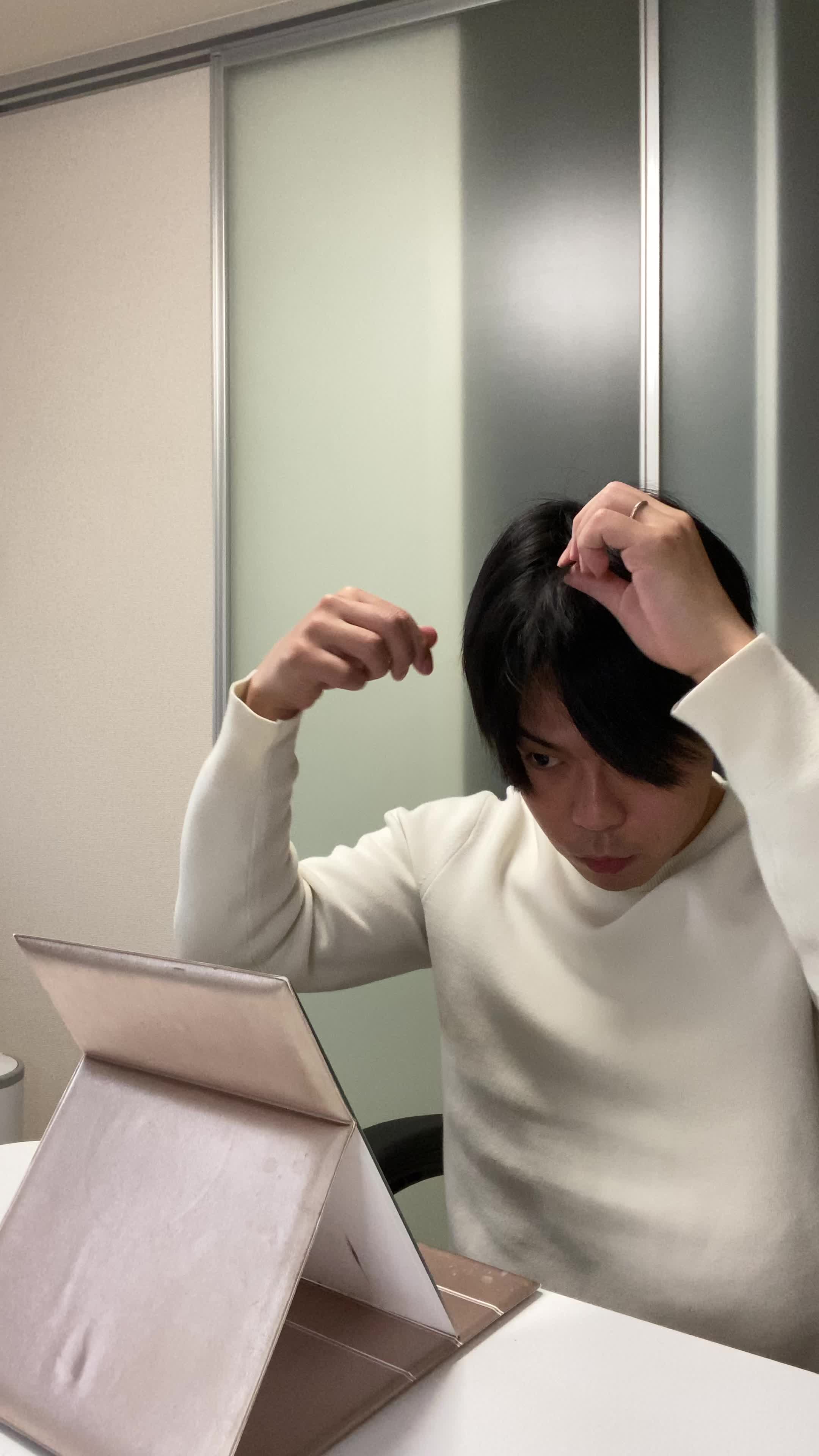 椅子に浅く腰掛け、鏡の前で「白髪部分を少し整える」動作