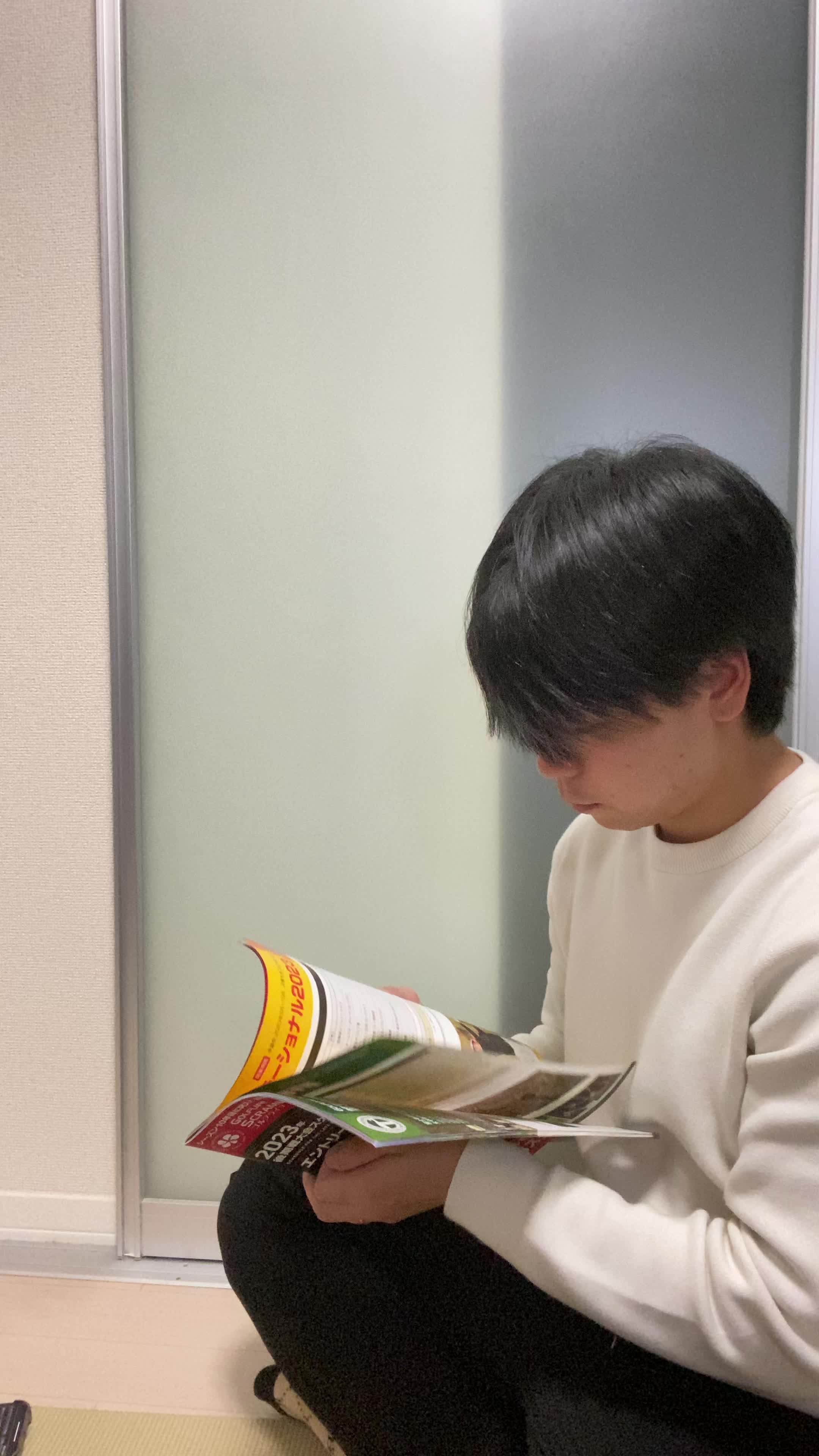 床でカタログを眺め、「白髪ケアの商品をじっくり選んでいる」様子