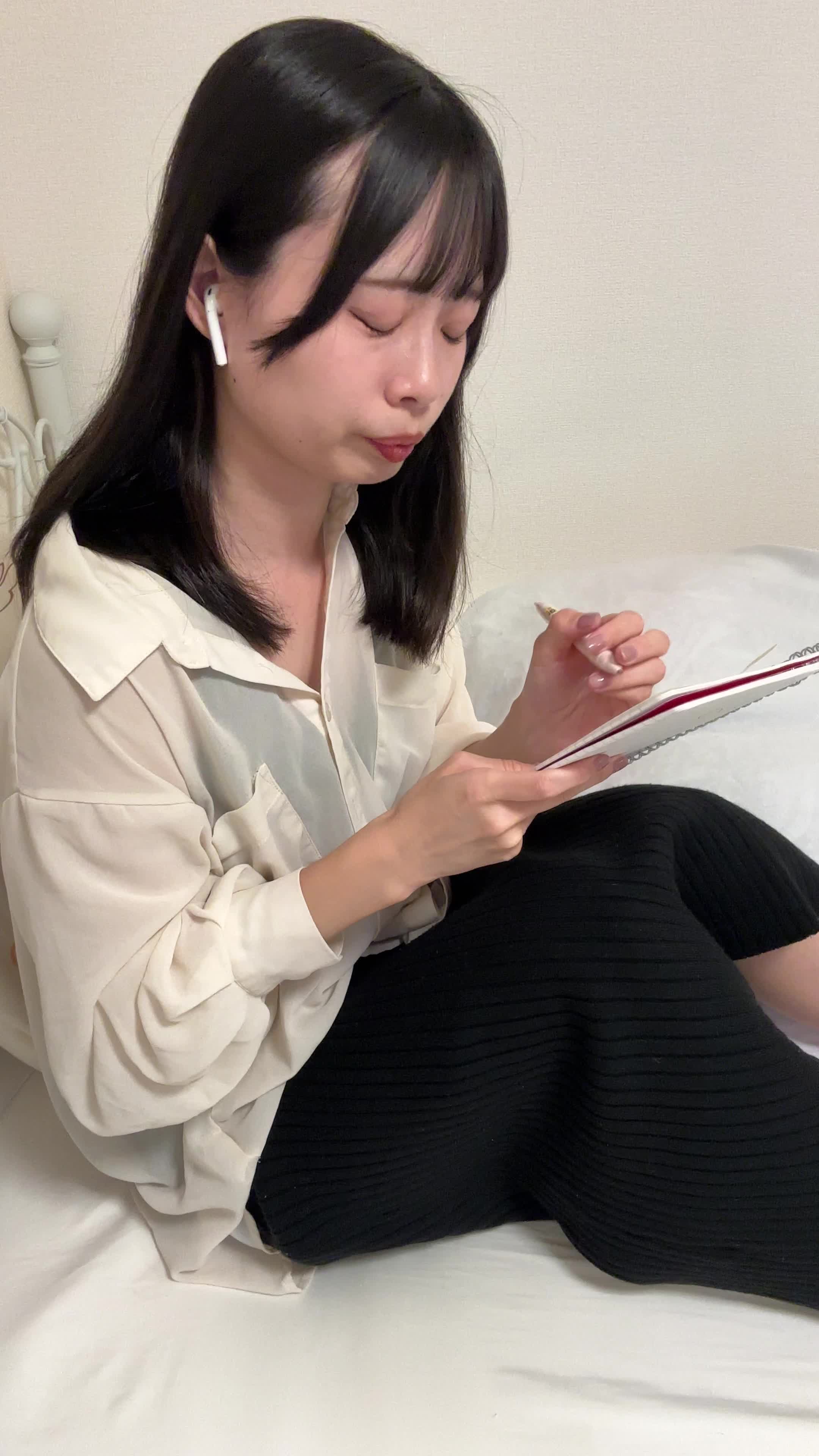 ベッドに横になり、イヤホンで音声を聞きながらメモを取ろうとする様子