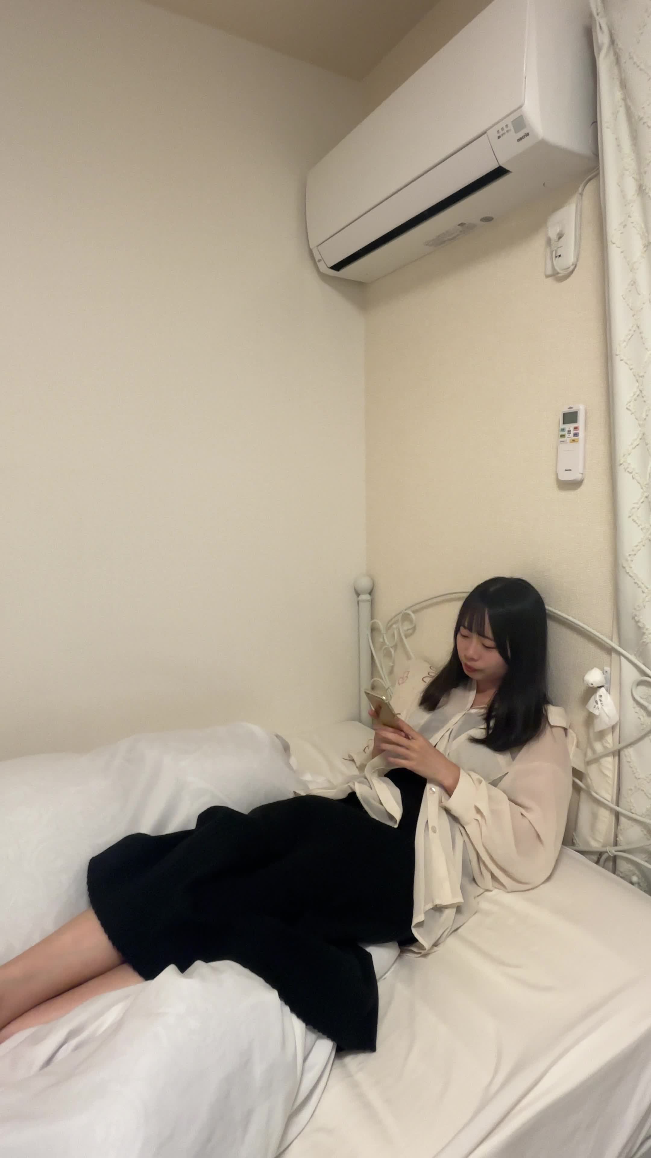 ベッドで脚を伸ばし、スマホでクイズアプリを操作しながら笑顔を浮かべる表情