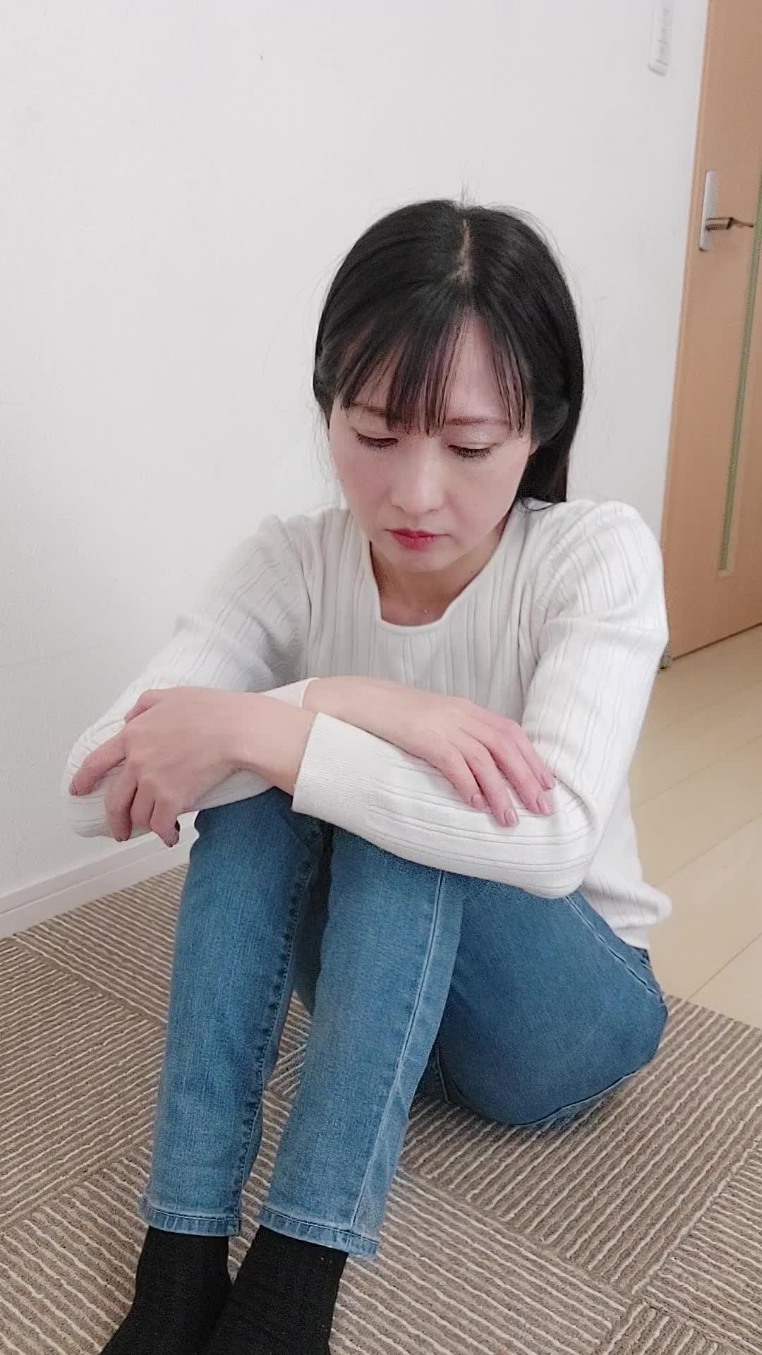 床で膝を抱え、「笑顔にもっと自信が持てるようになりたい」と考え込む様子