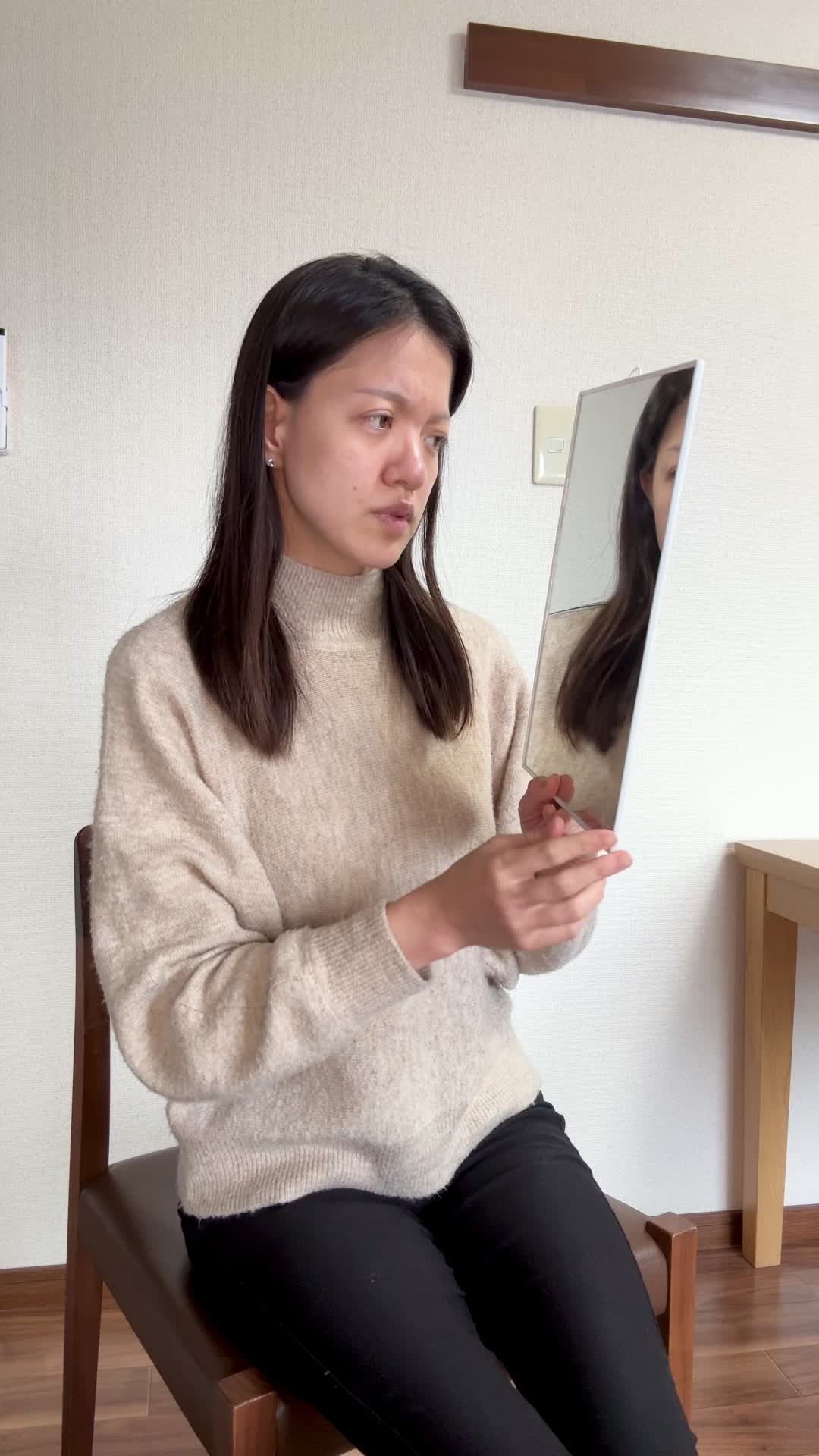 椅子に座り、鏡を見ながら白髪を気にして「どうにかならないかな」と悩む表情