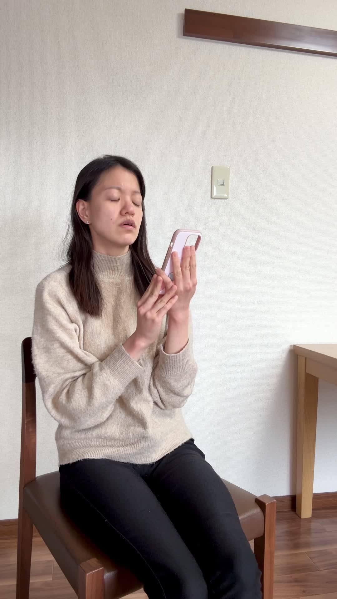 椅子に腰掛け、スマホの画面を見て「白髪ケアの口コミを読んで納得する」表情