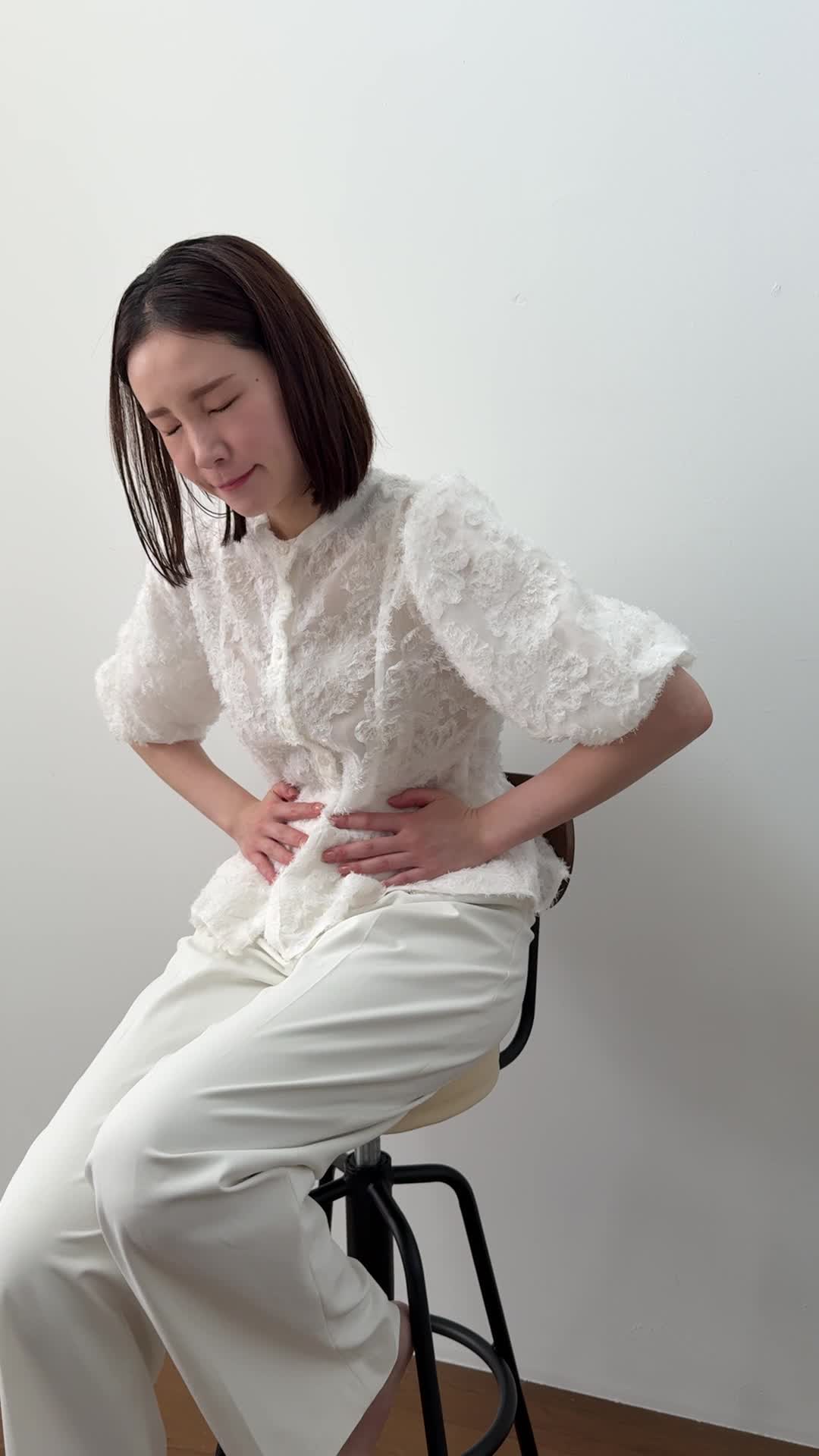 椅子に座り、お腹を軽く押さえながら「ずっと痛みが続いている…」と苦しそうな表情