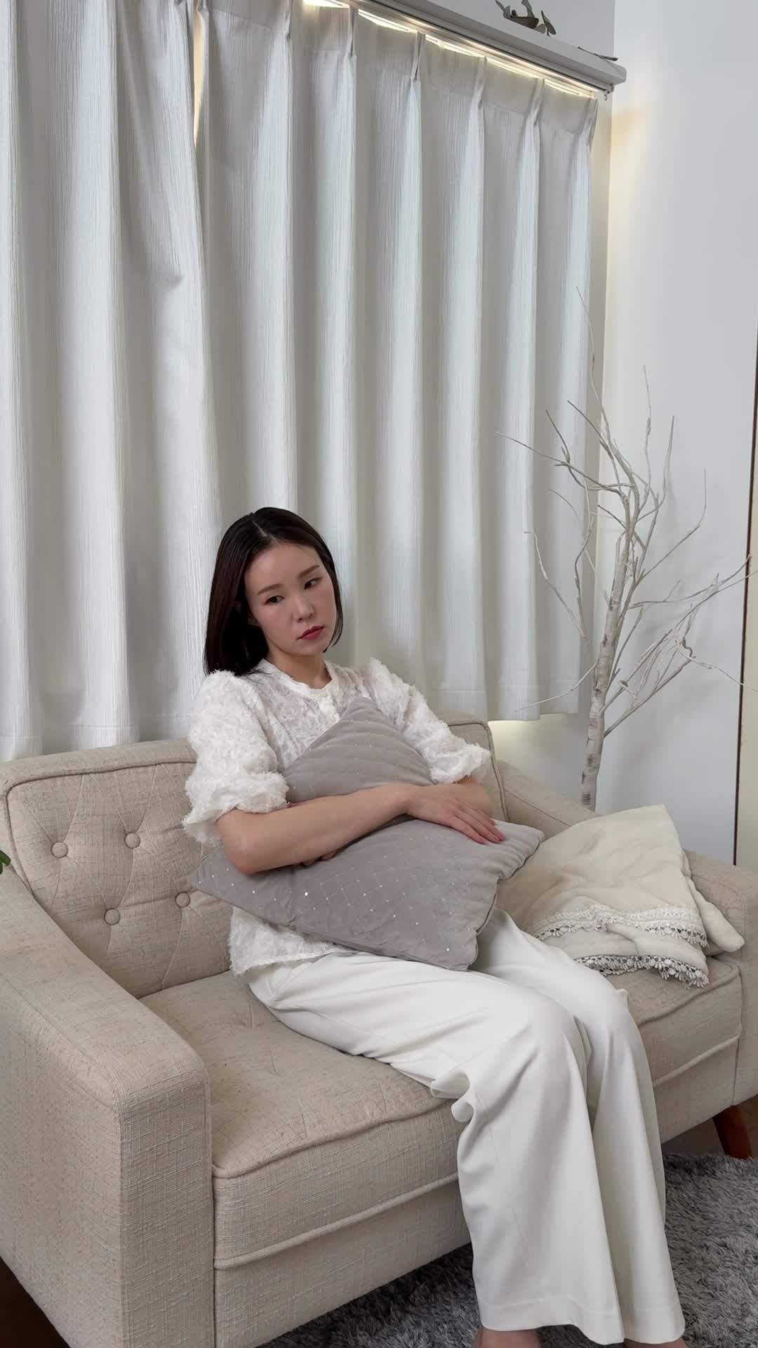 ソファでクッションを抱え、「腸が動いていない感じがして不安そうに考える」表情