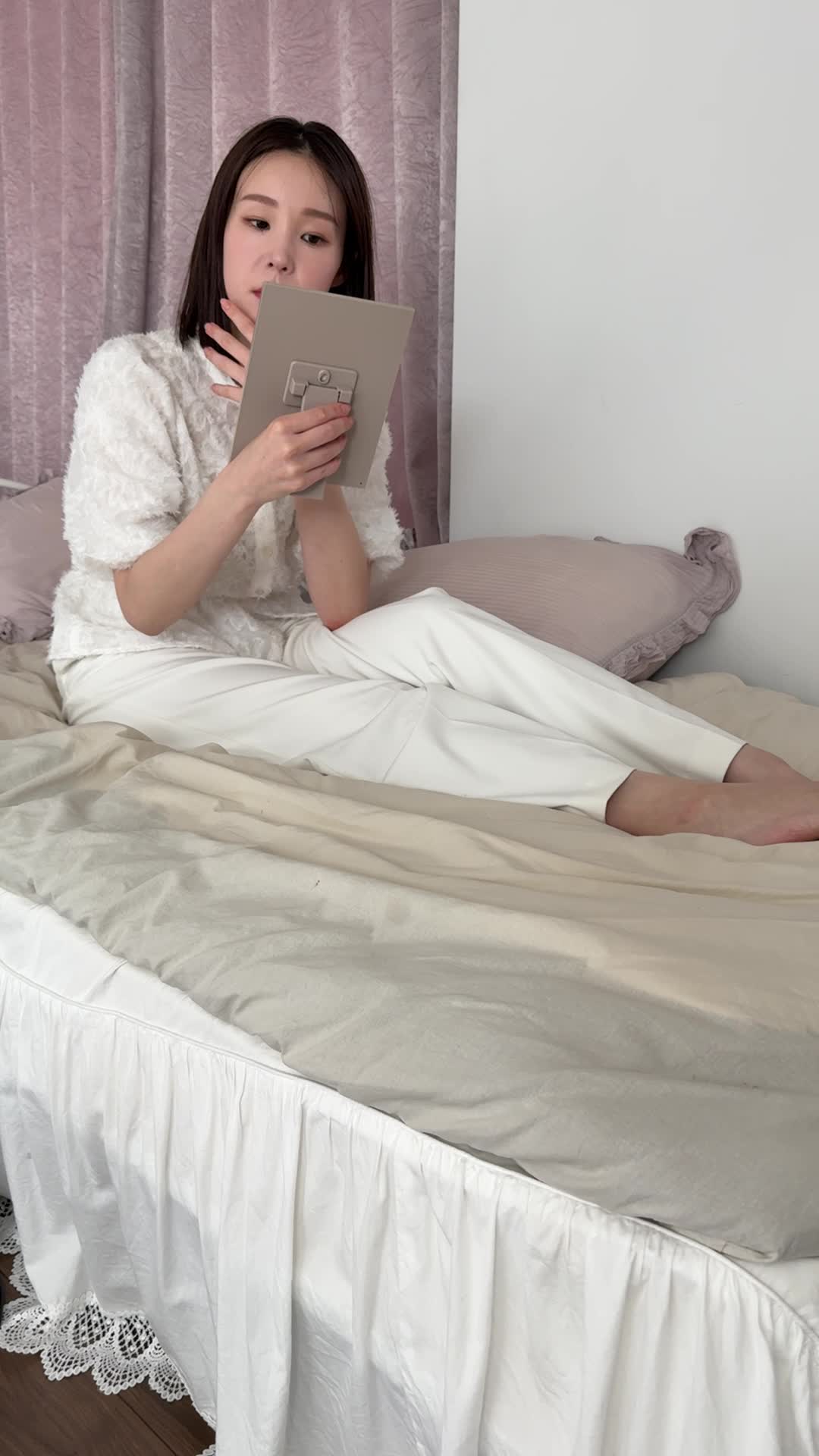 ベッドで脚を伸ばし、「便秘が原因で肌荒れしている気がする…」と鏡を見つめる動作