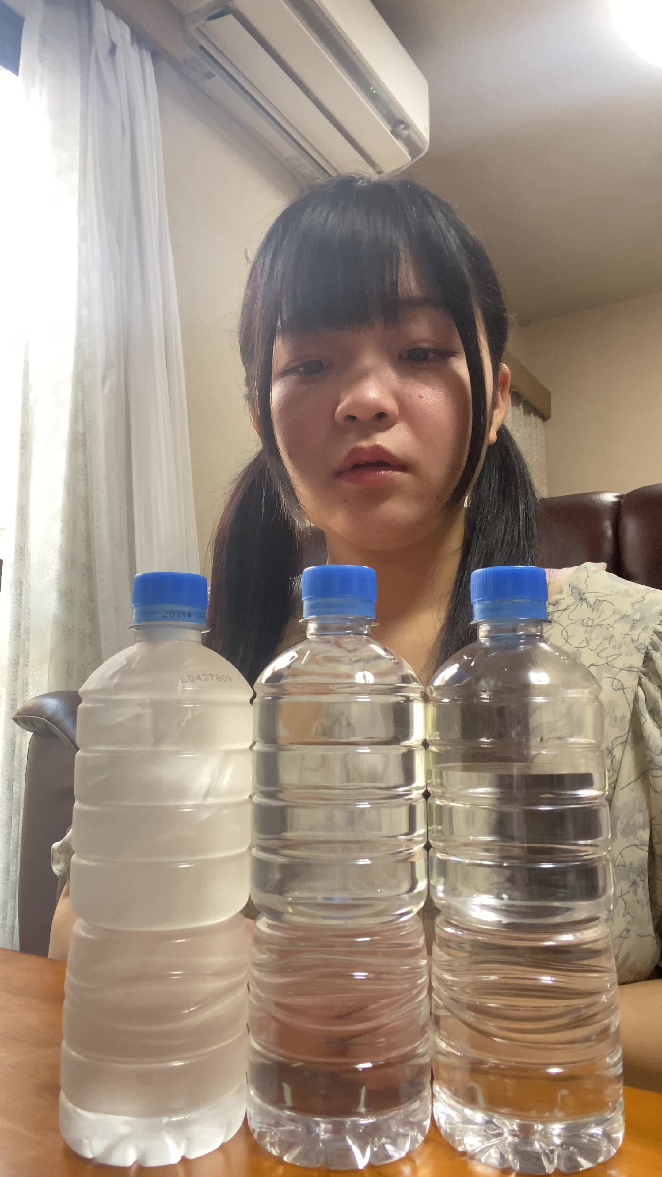 床に座り込み、スーパーの水のボトルを並べて「これを買い続けるのは大変」とため息をつく表情