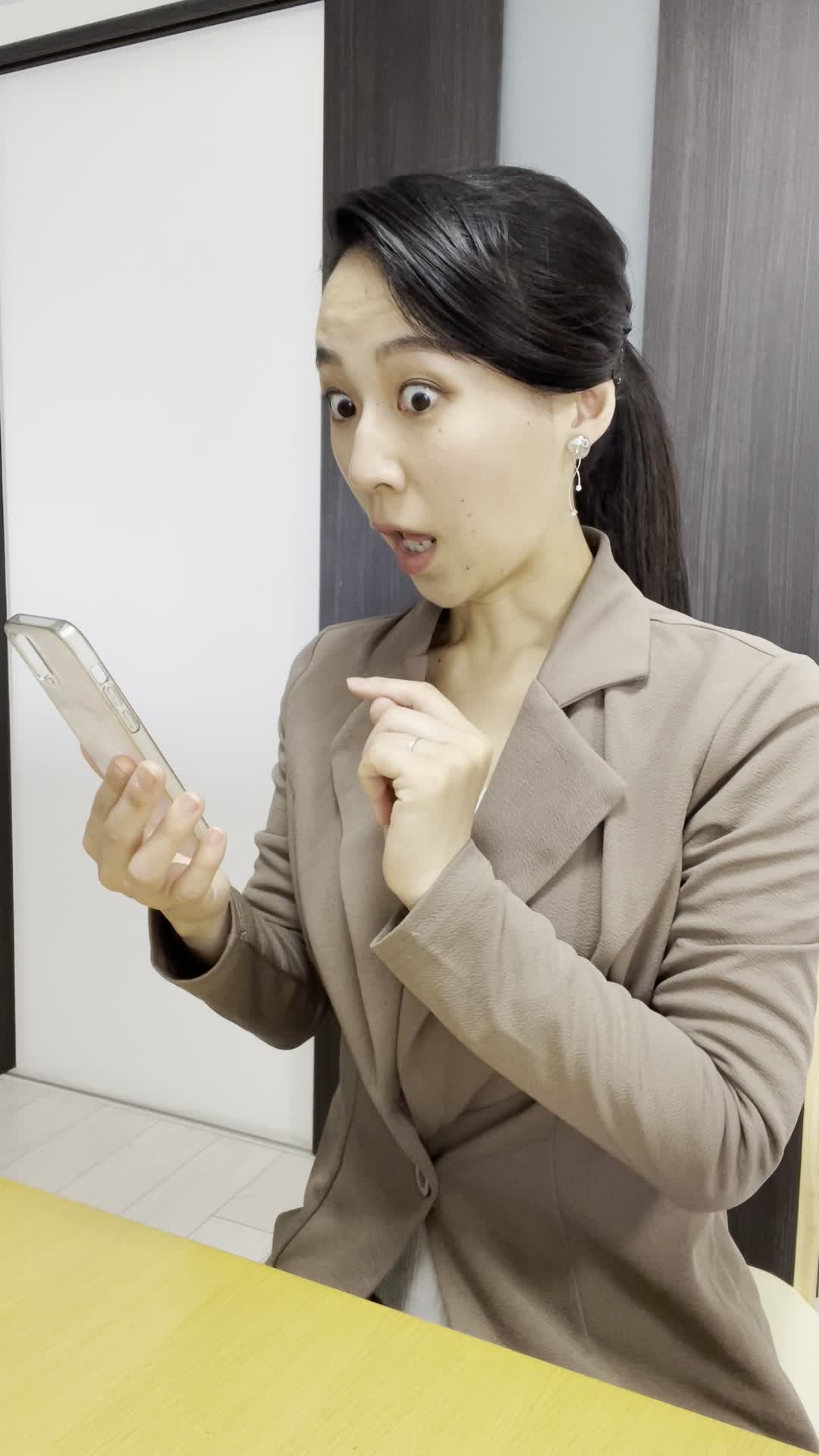 椅子に腰掛け、スマホで「ビフォーアフター写真」を見て驚きの表情を浮かべる姿