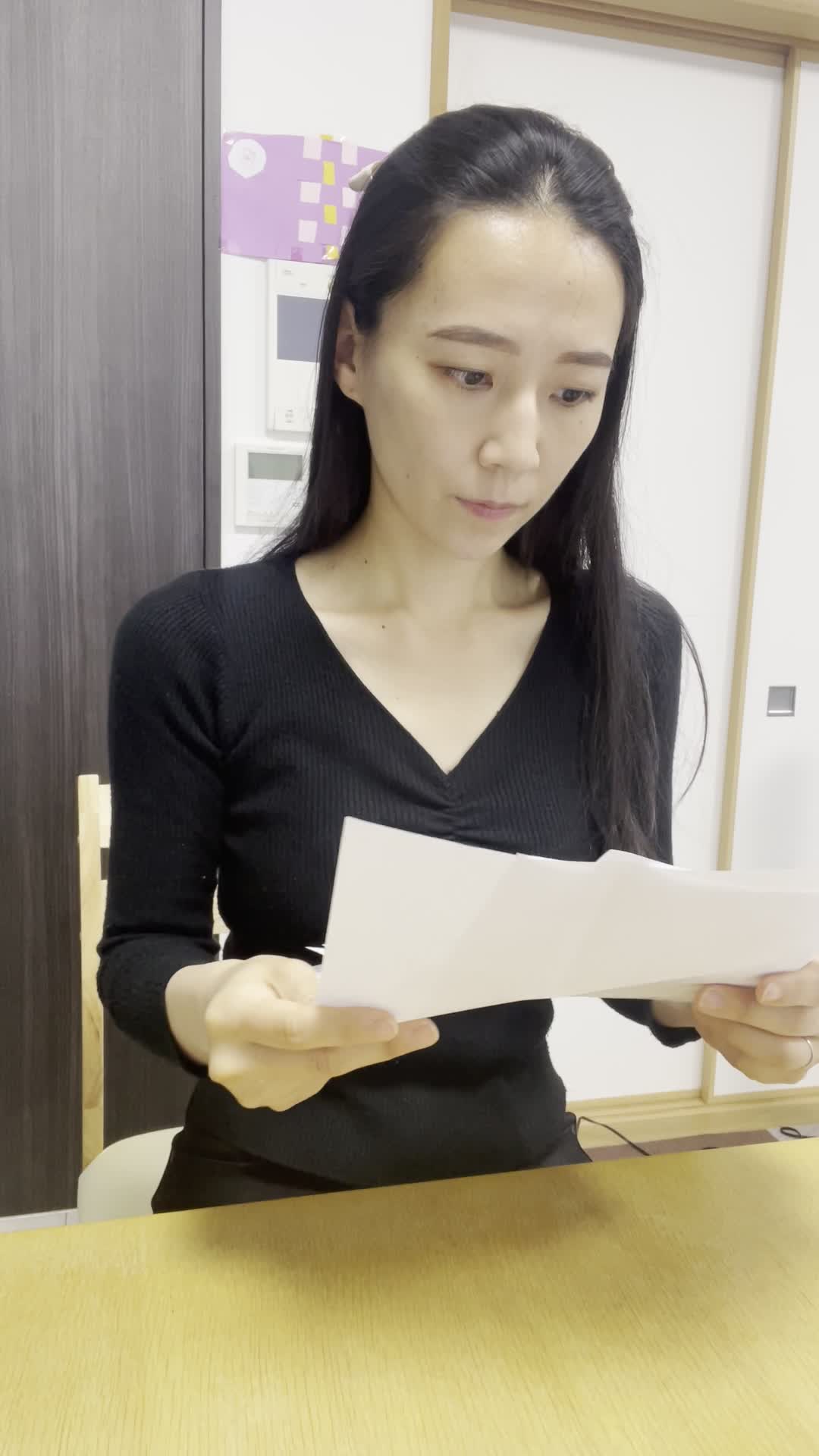 テーブルで紙をめくり、数字を指差しながら「これか！」と閃いた表情を浮かべる姿