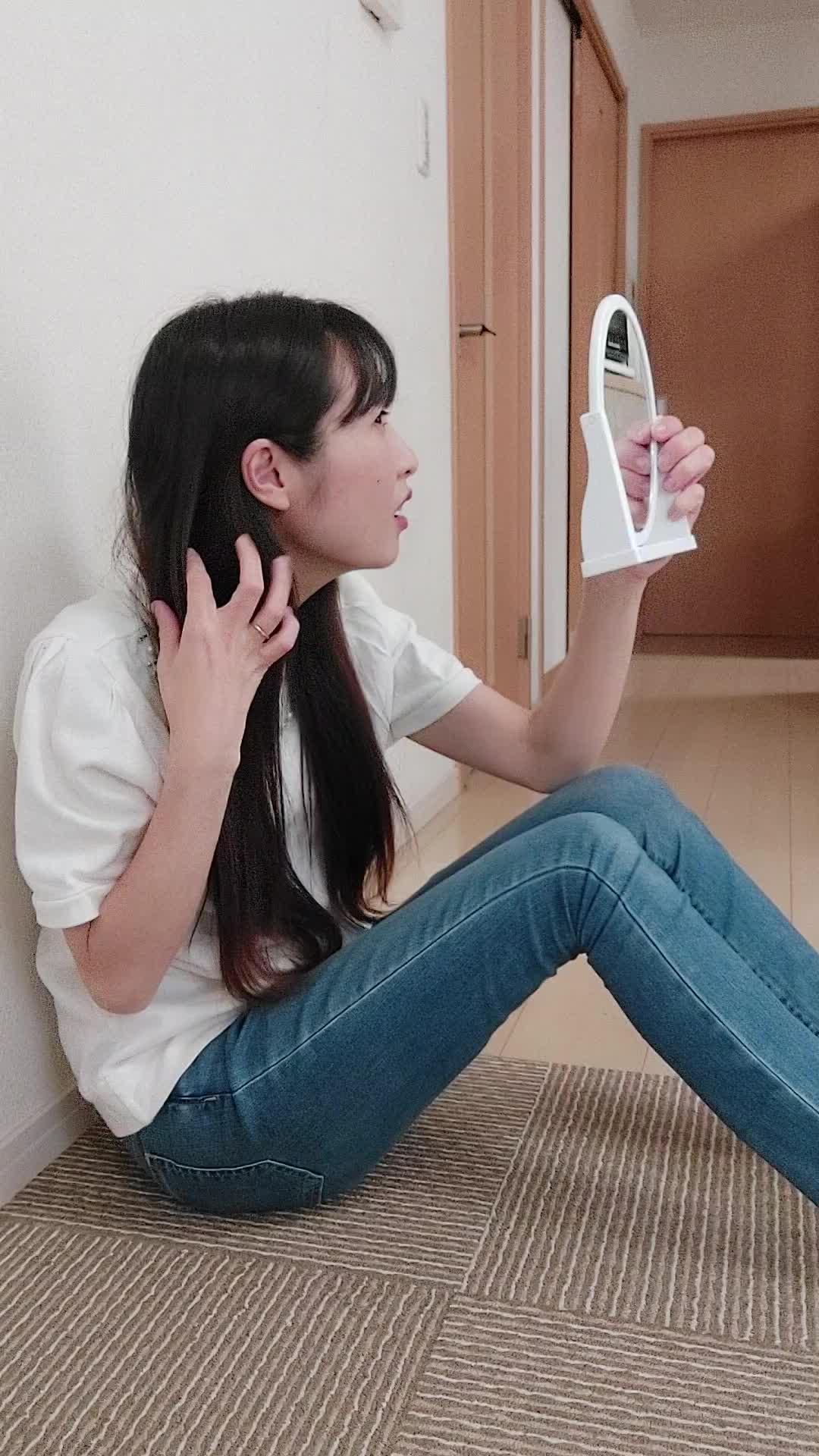 床に座り込み、鏡を近づけて白髪をじっくり確認し、「これがなくなれば…」と考える仕草