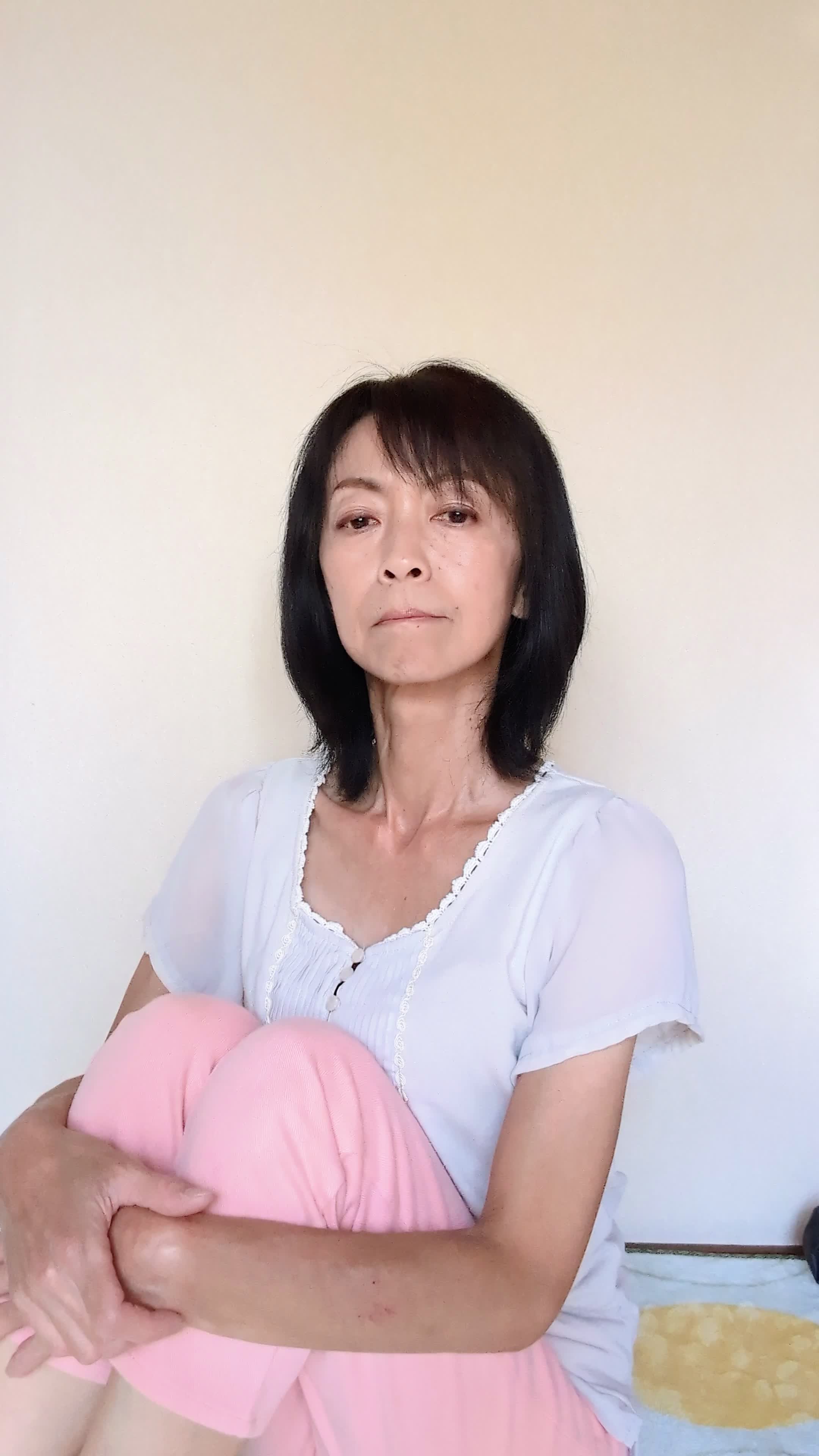 床で膝を抱え、「笑顔にもっと自信が持てるようになりたい」と考え込む様子