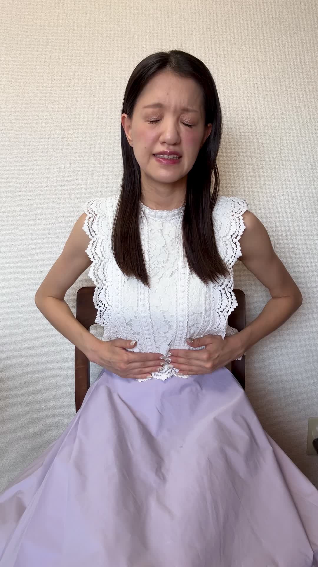 椅子に座り、お腹を軽く押さえながら「ずっと痛みが続いている…」と苦しそうな表情