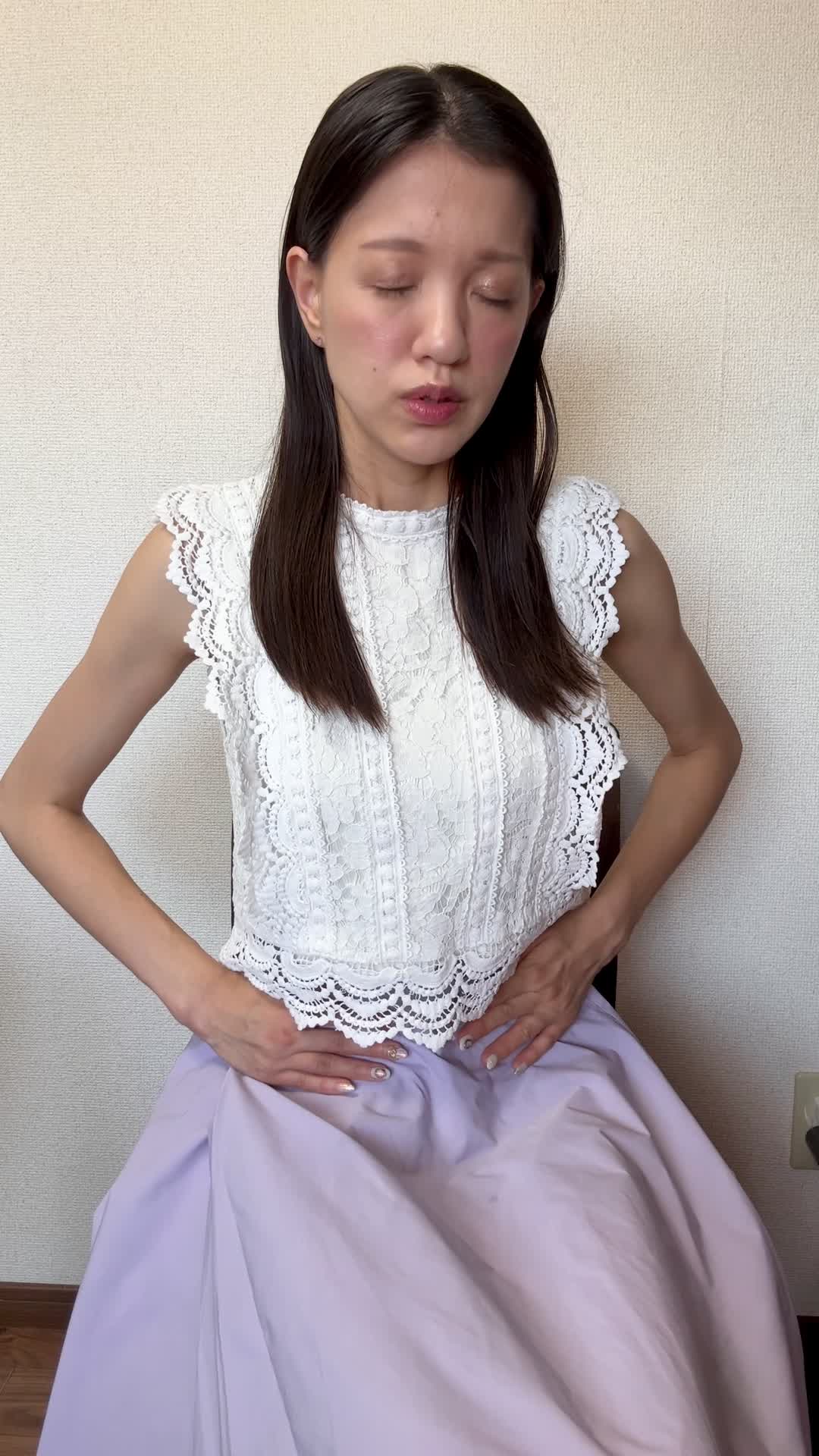 椅子に浅く腰掛け、「下腹部を両手で押さえて痛みを和らげようとする」動作