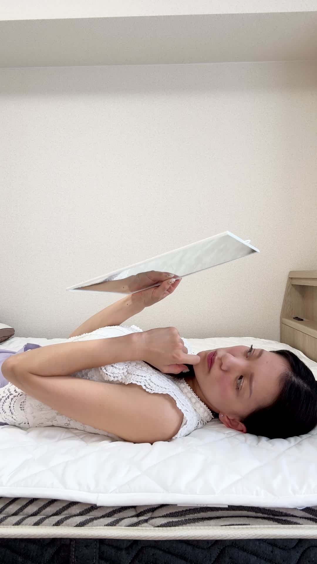 ベッドで脚を伸ばし、「便秘が原因で肌荒れしている気がする…」と鏡を見つめる動作