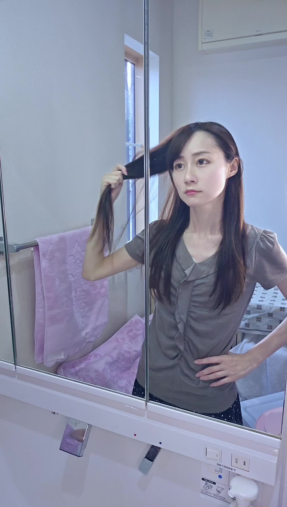 鏡を見つめながら、髪を軽く引っ張り状態を確認する仕草をする