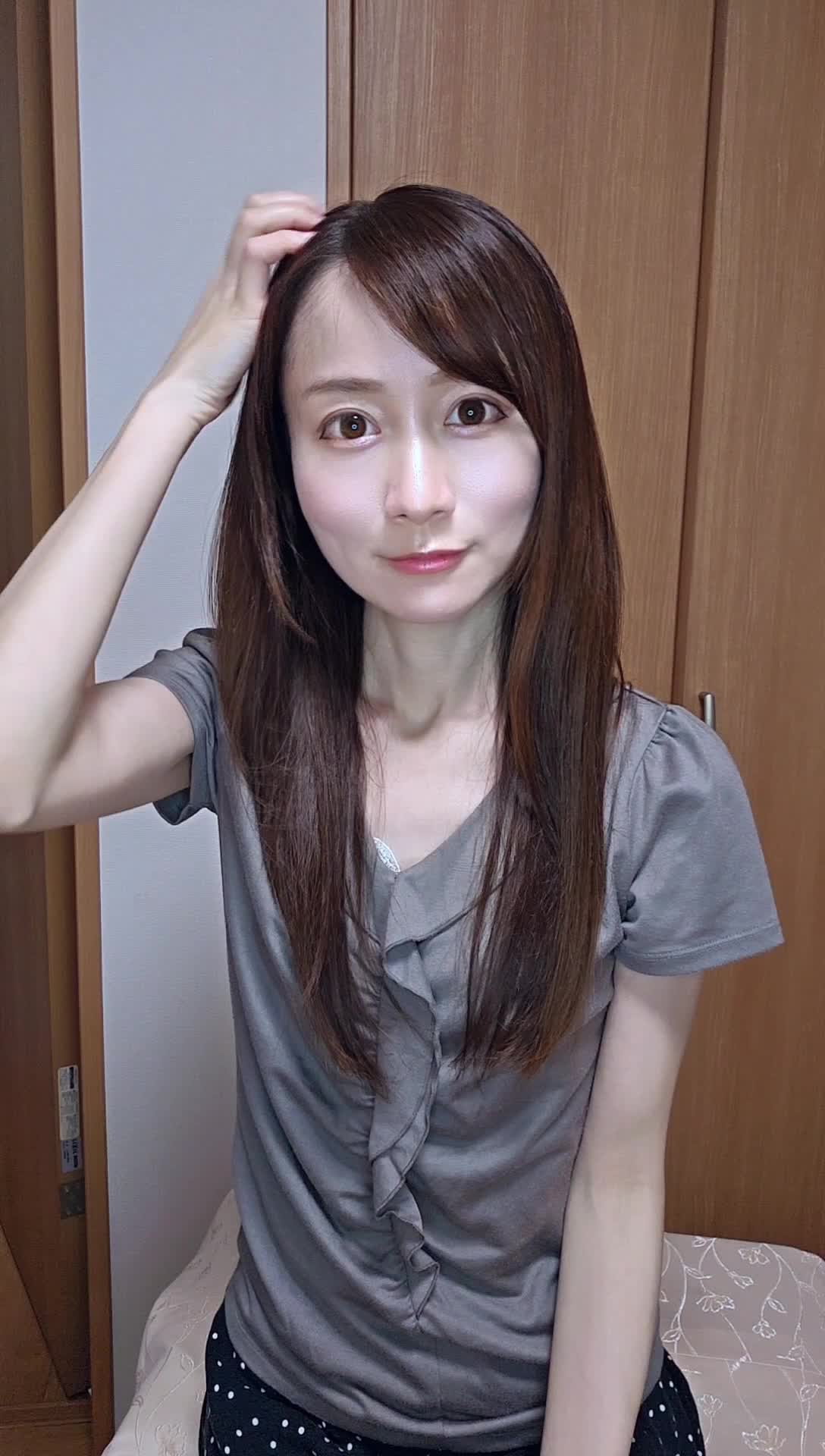 椅子に座りながら、手で髪を軽く整える自然な仕草をする