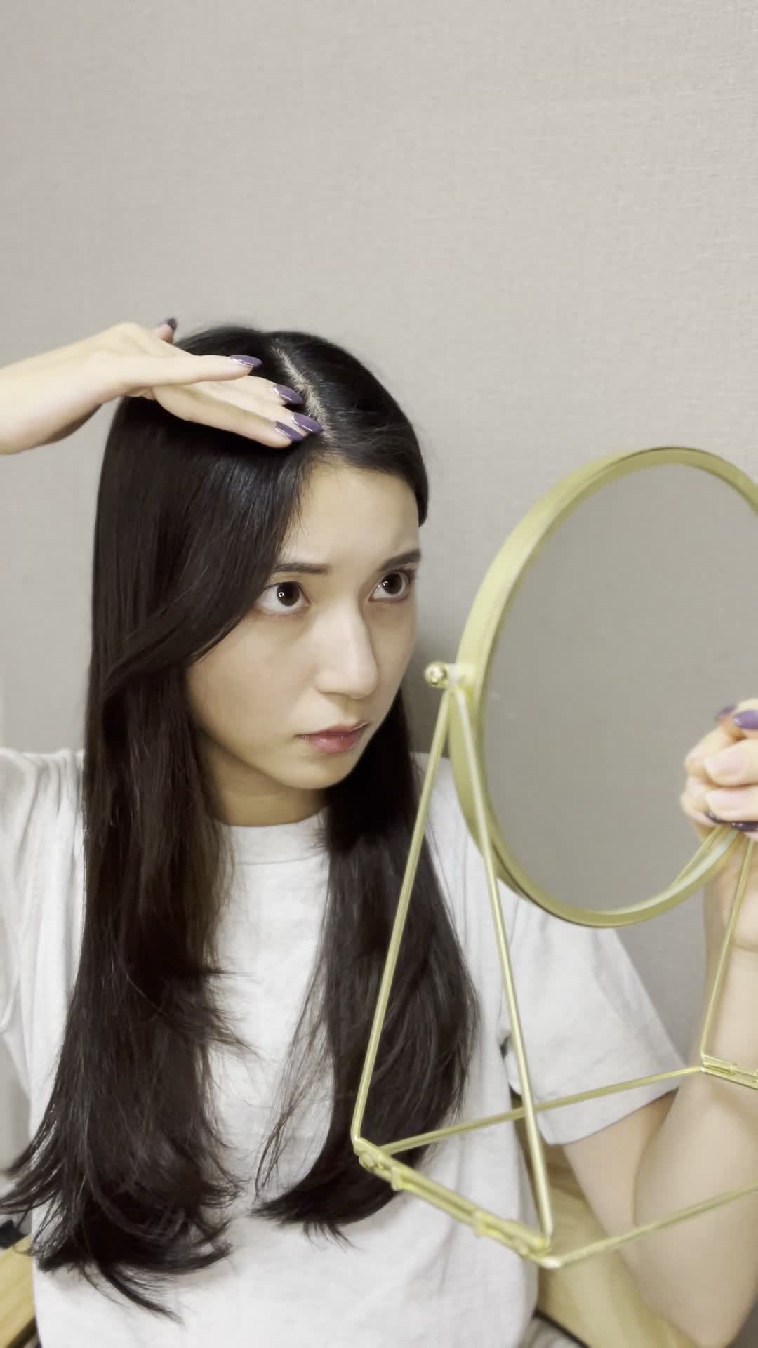 鏡の前で髪の分け目をじっと観察しながら少し真剣な表情を見せる