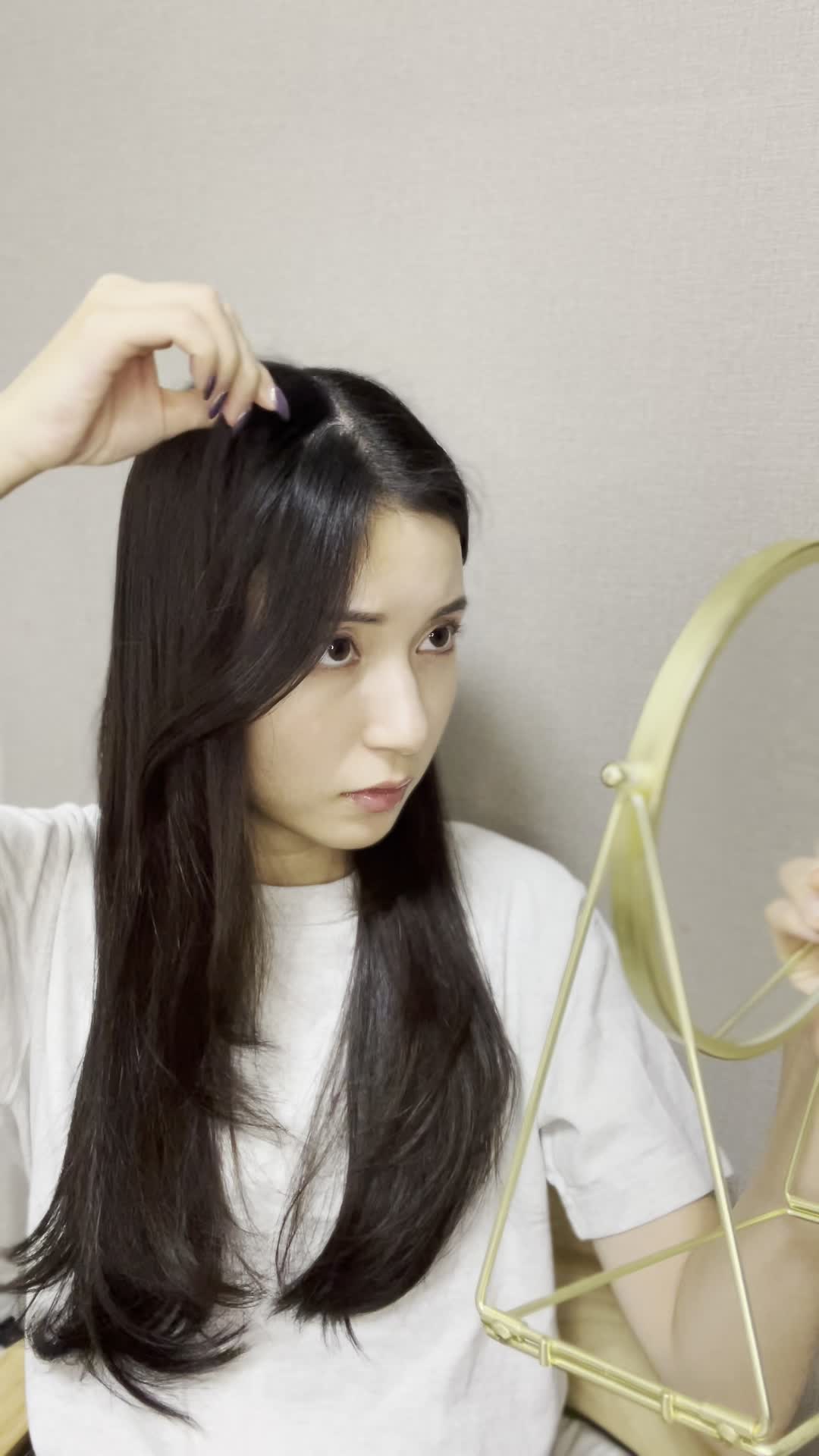 鏡を見つめながら、髪を軽く引っ張り状態を確認する仕草をする