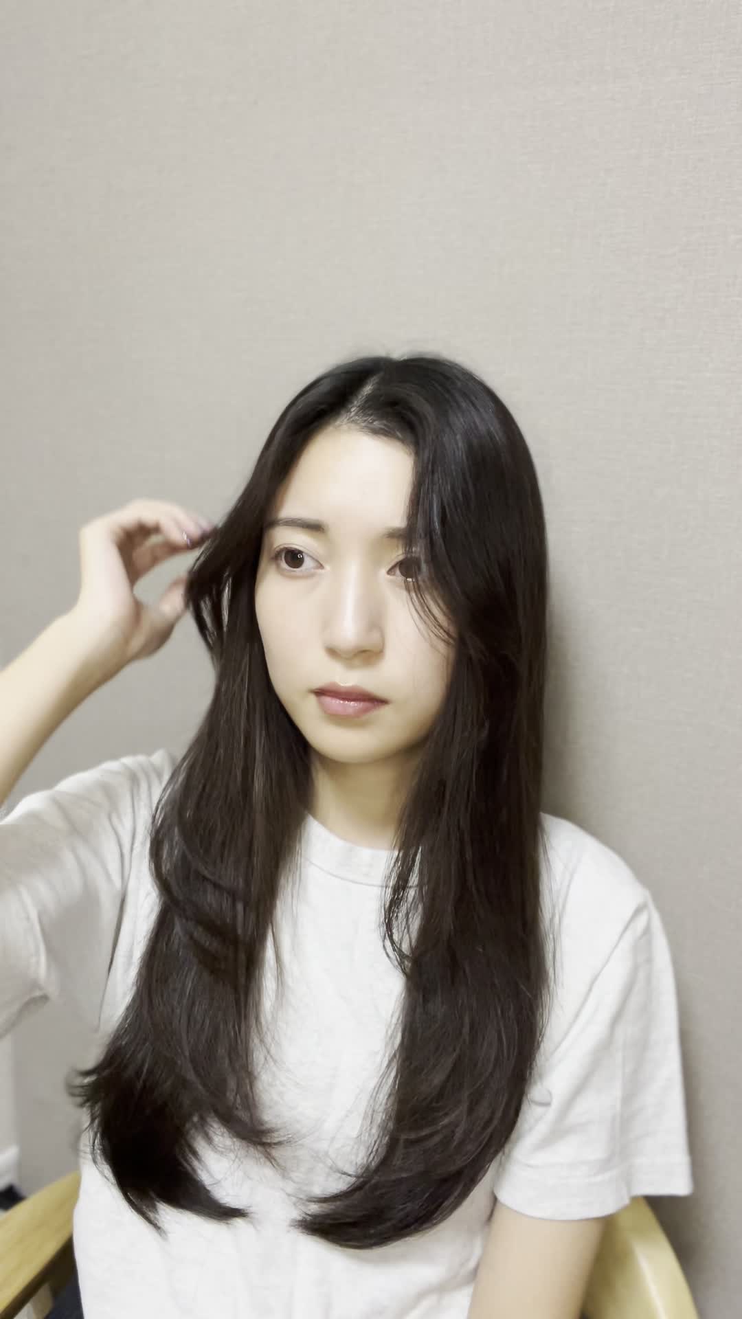 椅子に座りながら、手で髪を軽く整える自然な仕草をする