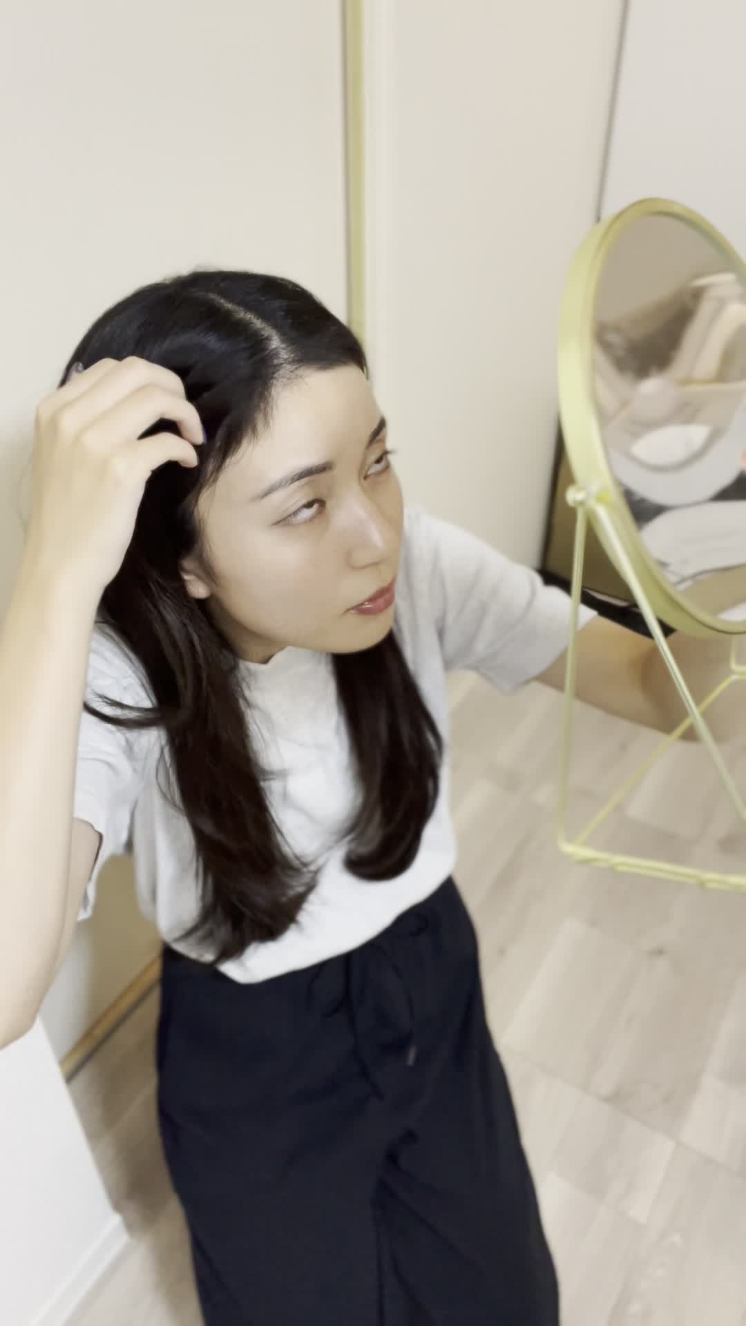 床に膝をつき、鏡を持って頭頂部を確認する仕草をする