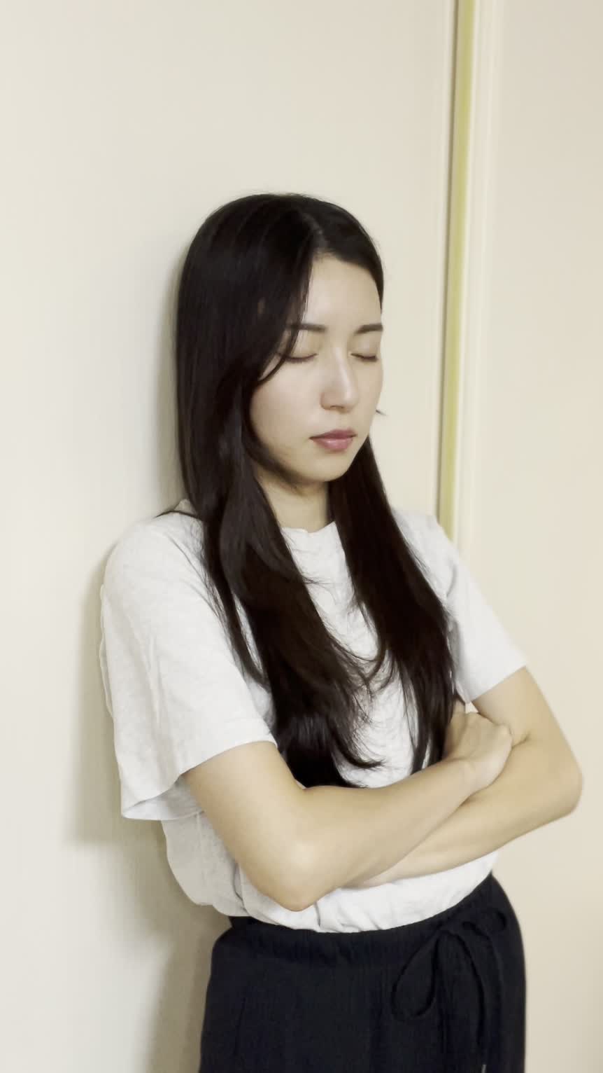 壁に背を預けて静かに目を閉じ、悩みを抱えている仕草をする