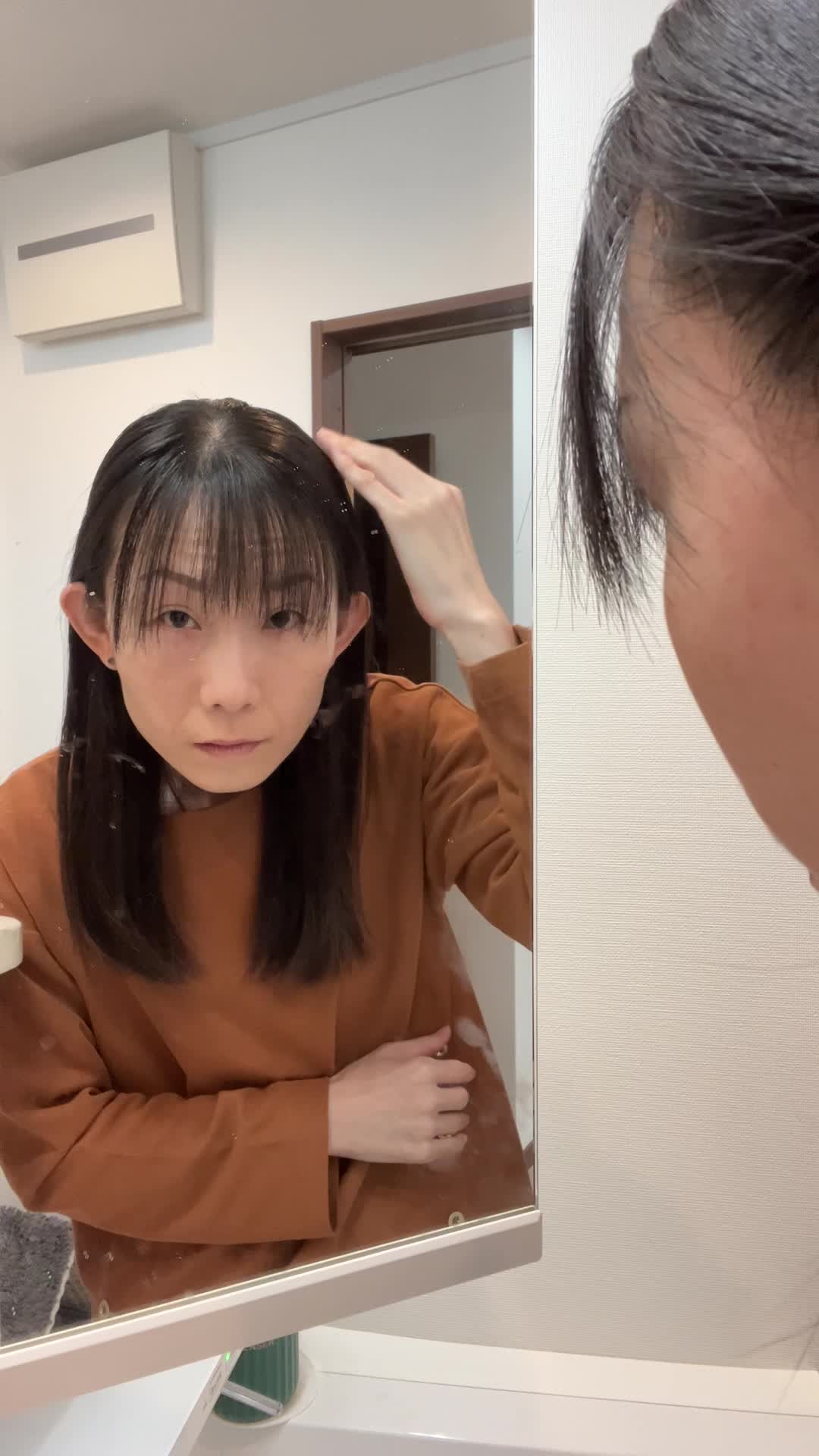 鏡の前で髪の分け目をじっと観察しながら少し真剣な表情を見せる