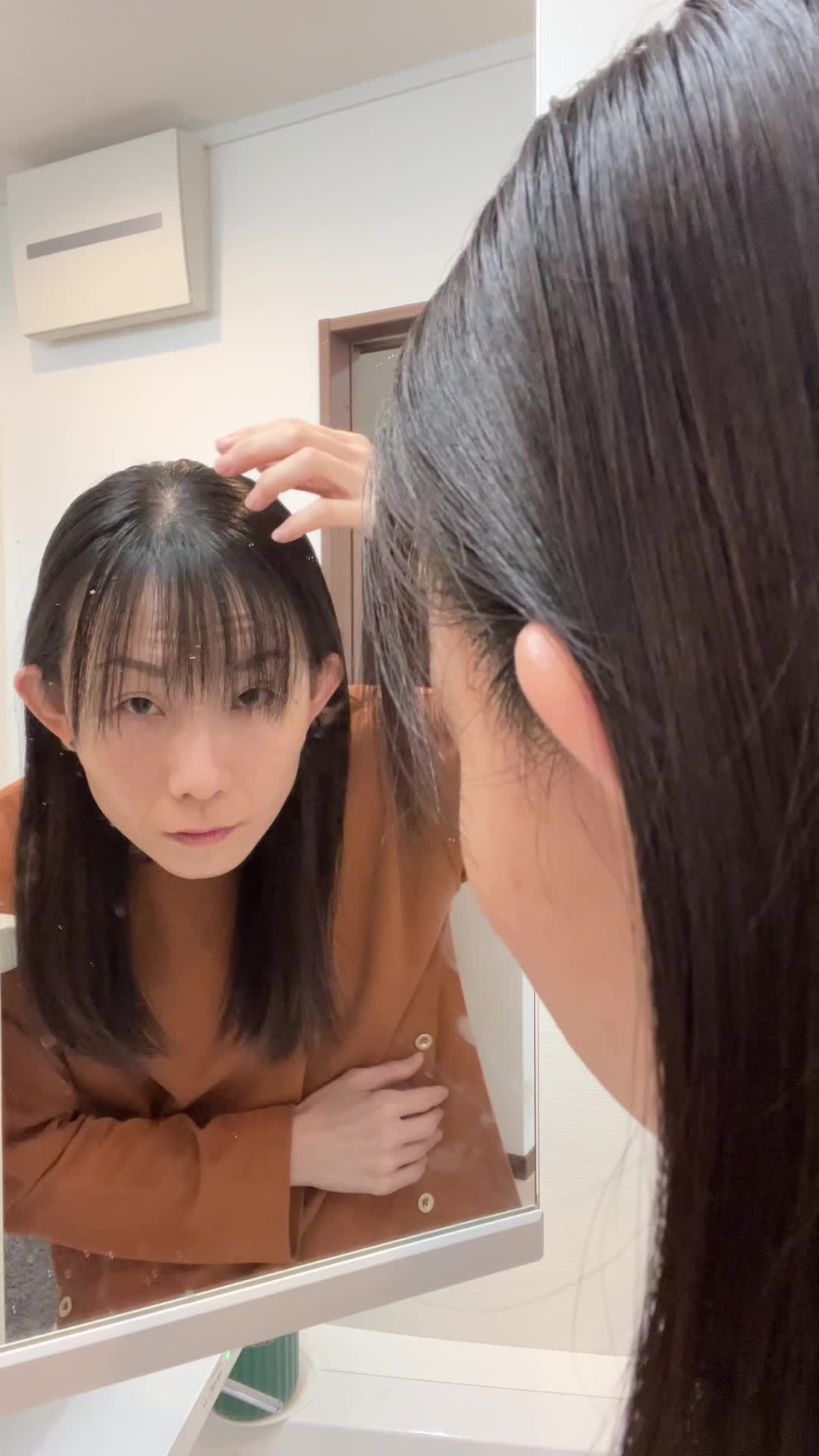 鏡を見つめながら、髪を軽く引っ張り状態を確認する仕草をする