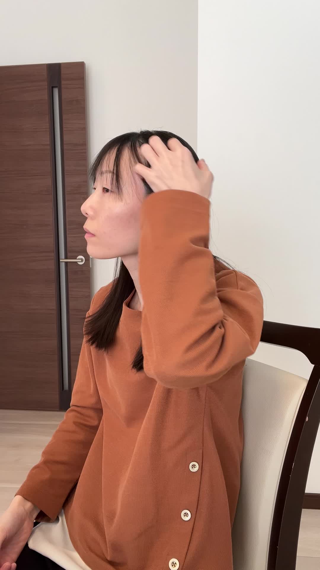 椅子に座りながら、手で髪を軽く整える自然な仕草をする