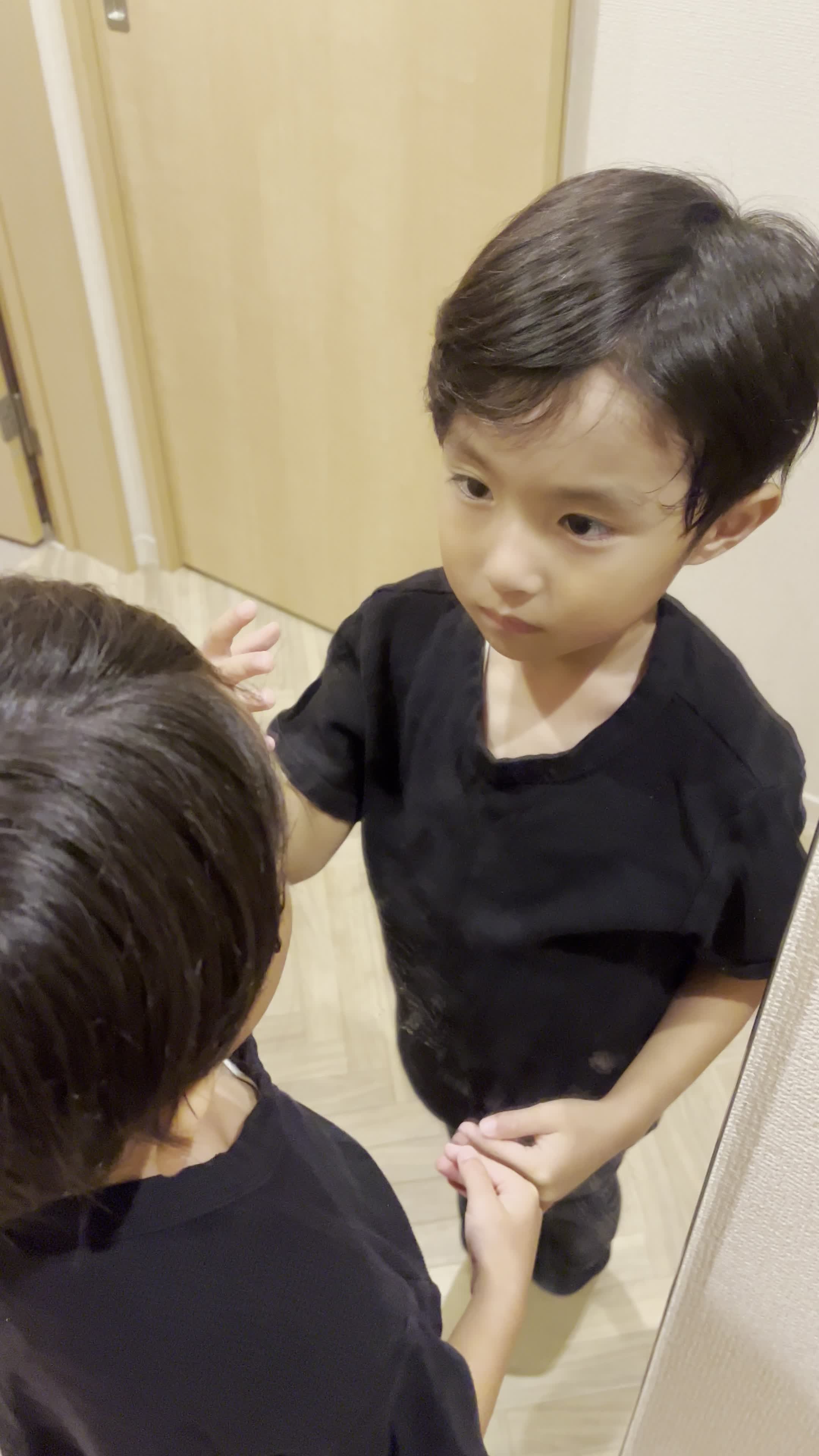 鏡の前で髪の分け目をじっと観察しながら少し真剣な表情を見せる