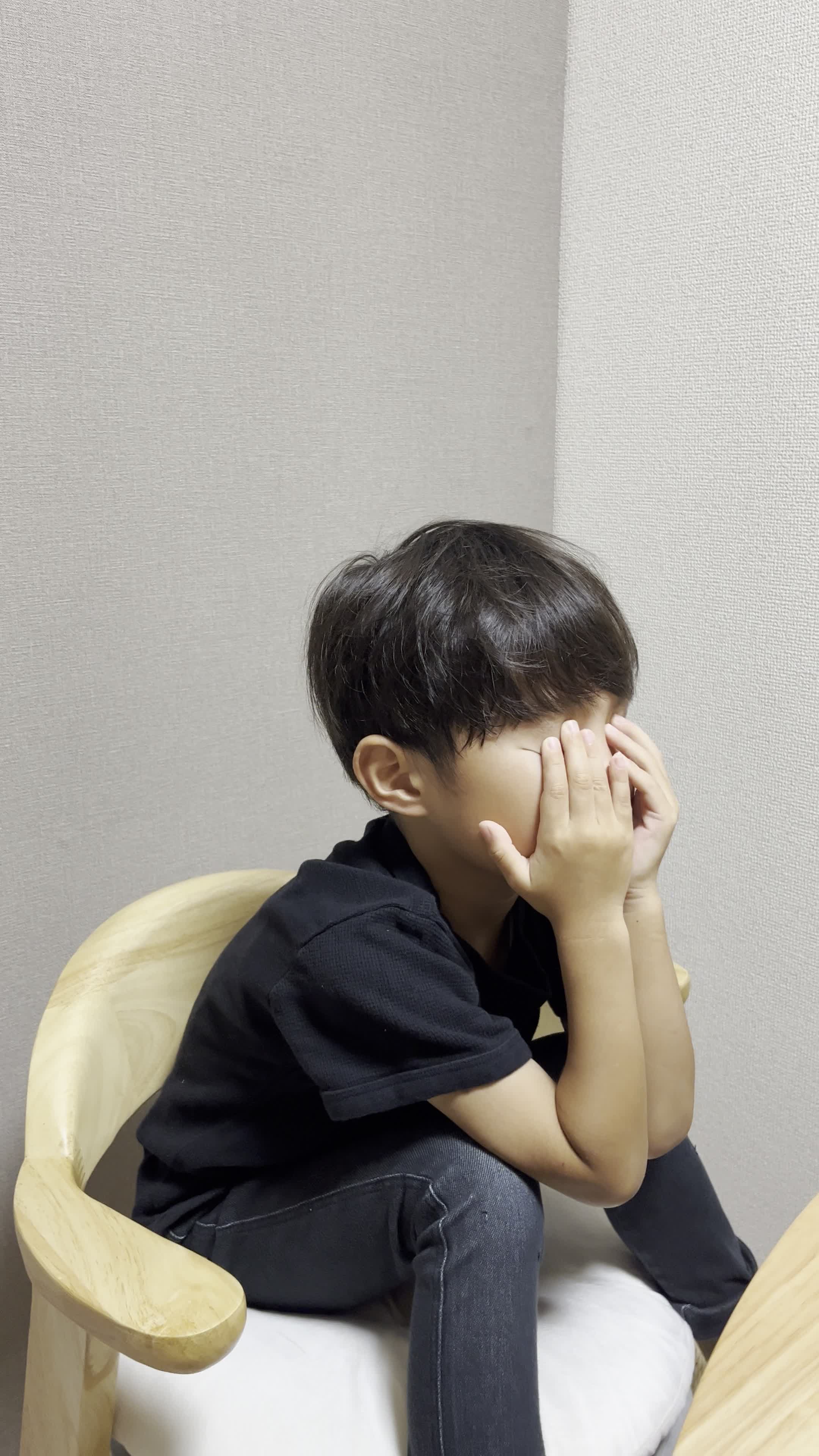 椅子に腰掛け、両手で顔を覆い、悩んでいる様子を表現する