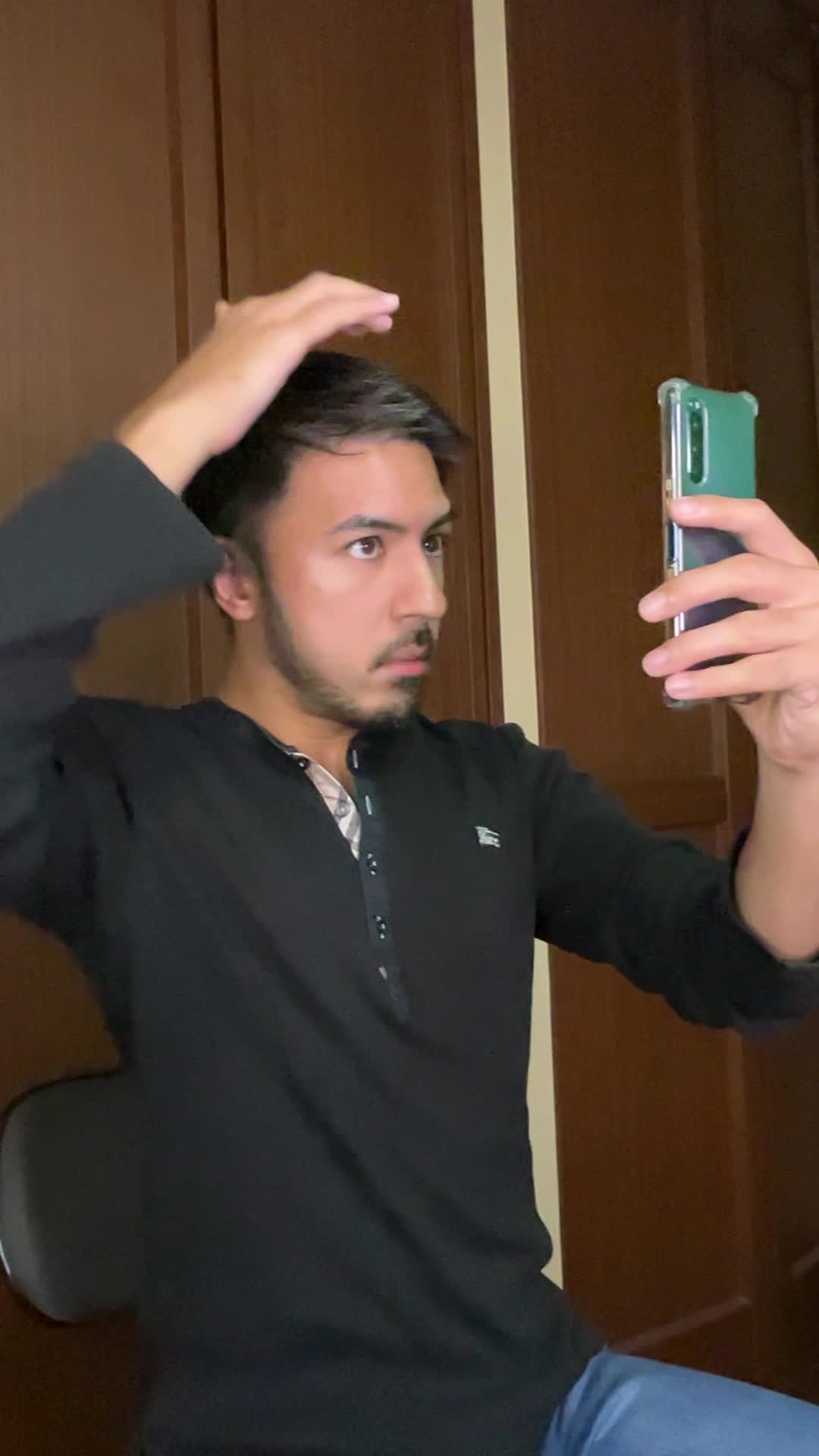 スマホで髪の分け目をじっと観察しながら少し真剣な表情を見せる