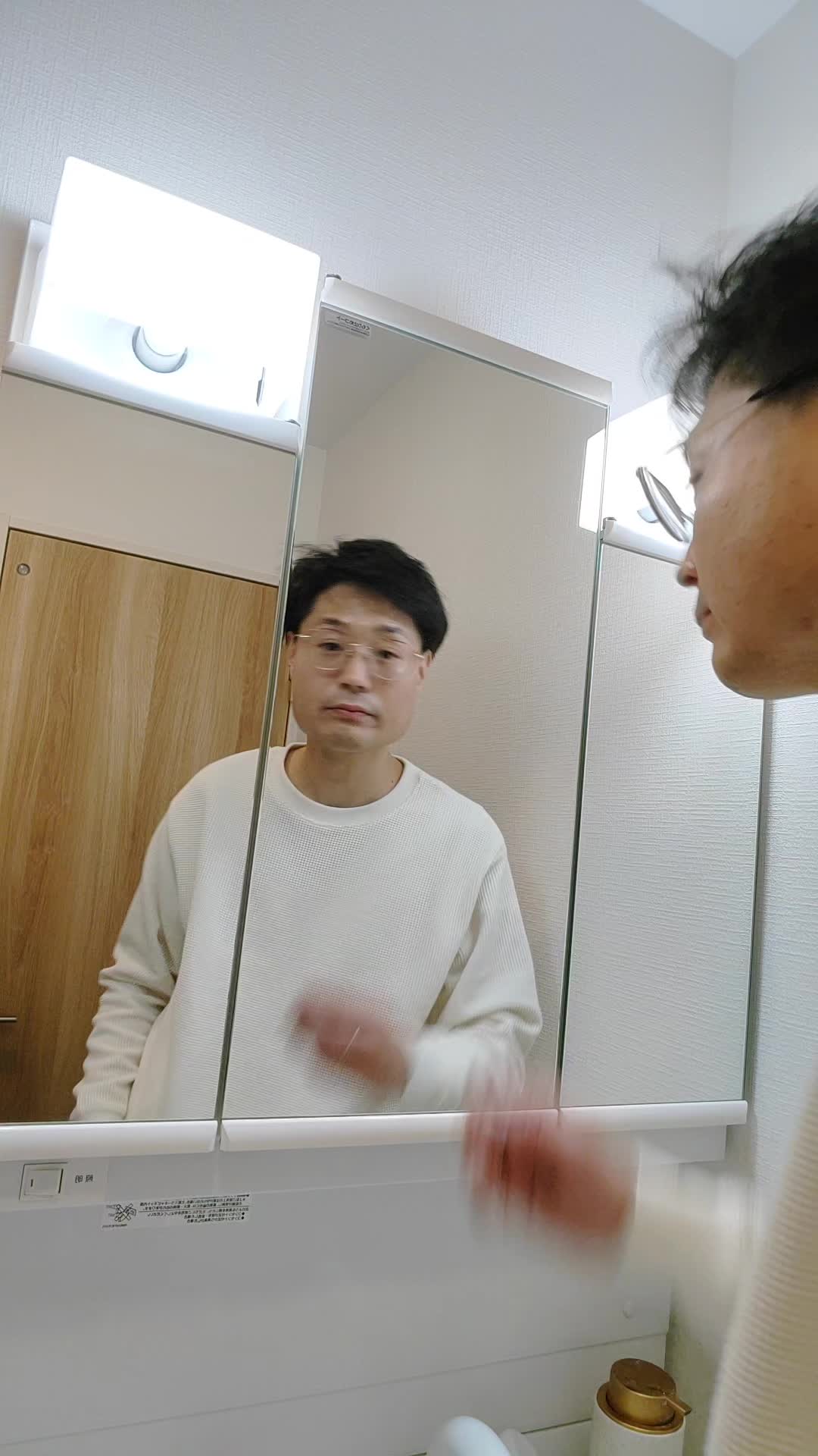 鏡の前で髪の分け目をじっと観察しながら少し真剣な表情を見せる