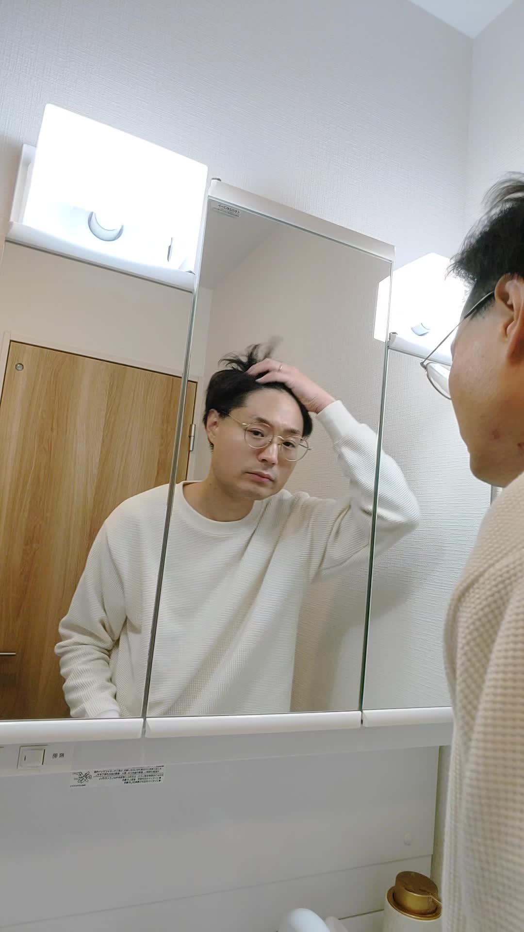 鏡を見つめながら、髪を軽く引っ張り状態を確認する仕草をする