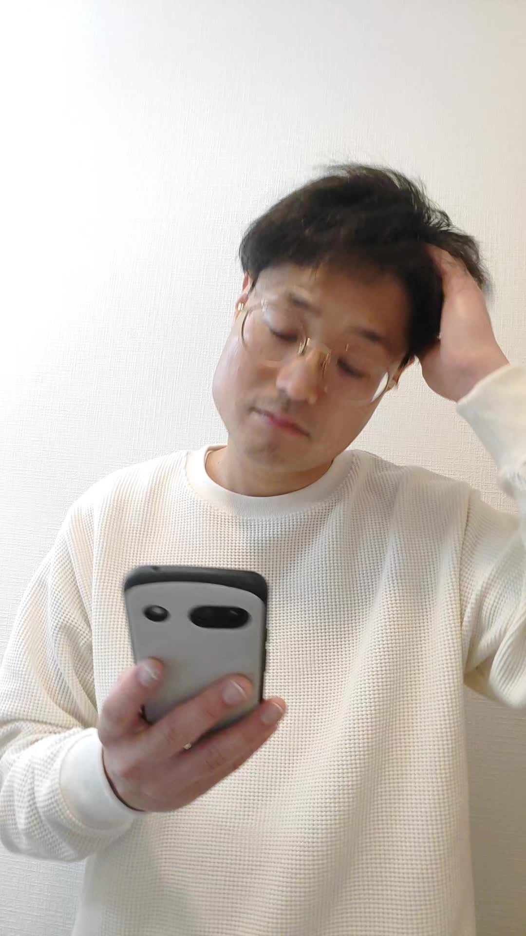 スマホを片手で持ち、もう片手で頭を触りながら考え込む