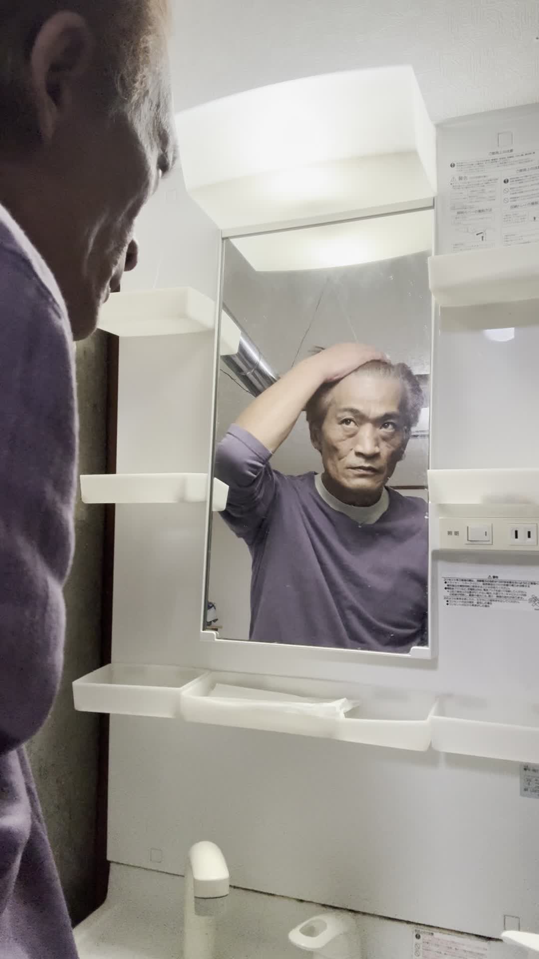 鏡の前で髪の分け目をじっと観察しながら少し真剣な表情を見せる