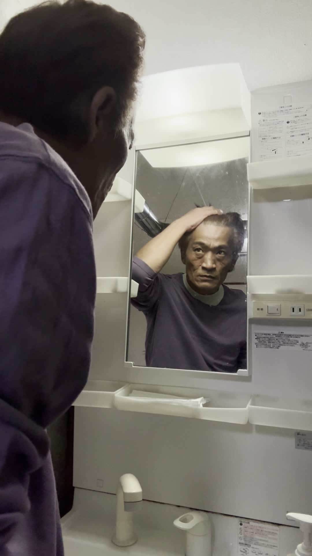 鏡を見つめながら、髪を軽く引っ張り状態を確認する仕草をする