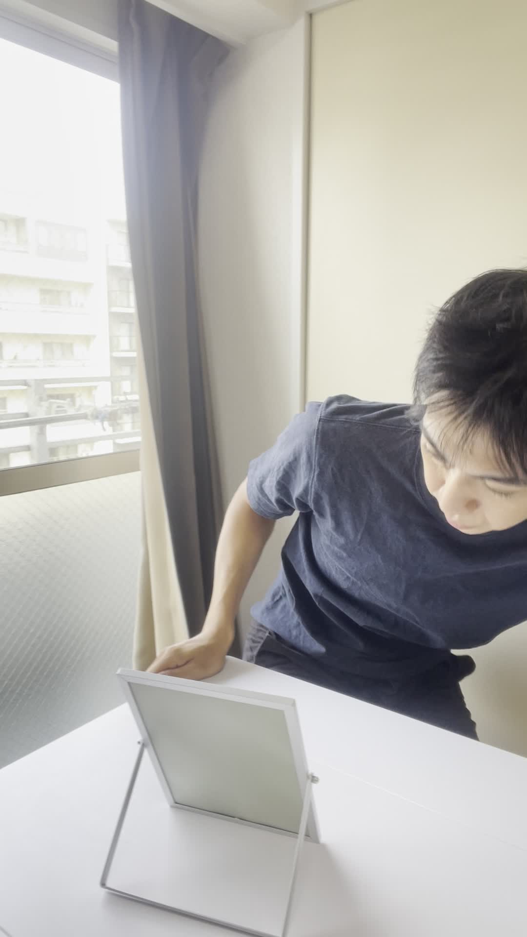 鏡を見つめながら、髪を軽く引っ張り状態を確認する仕草をする