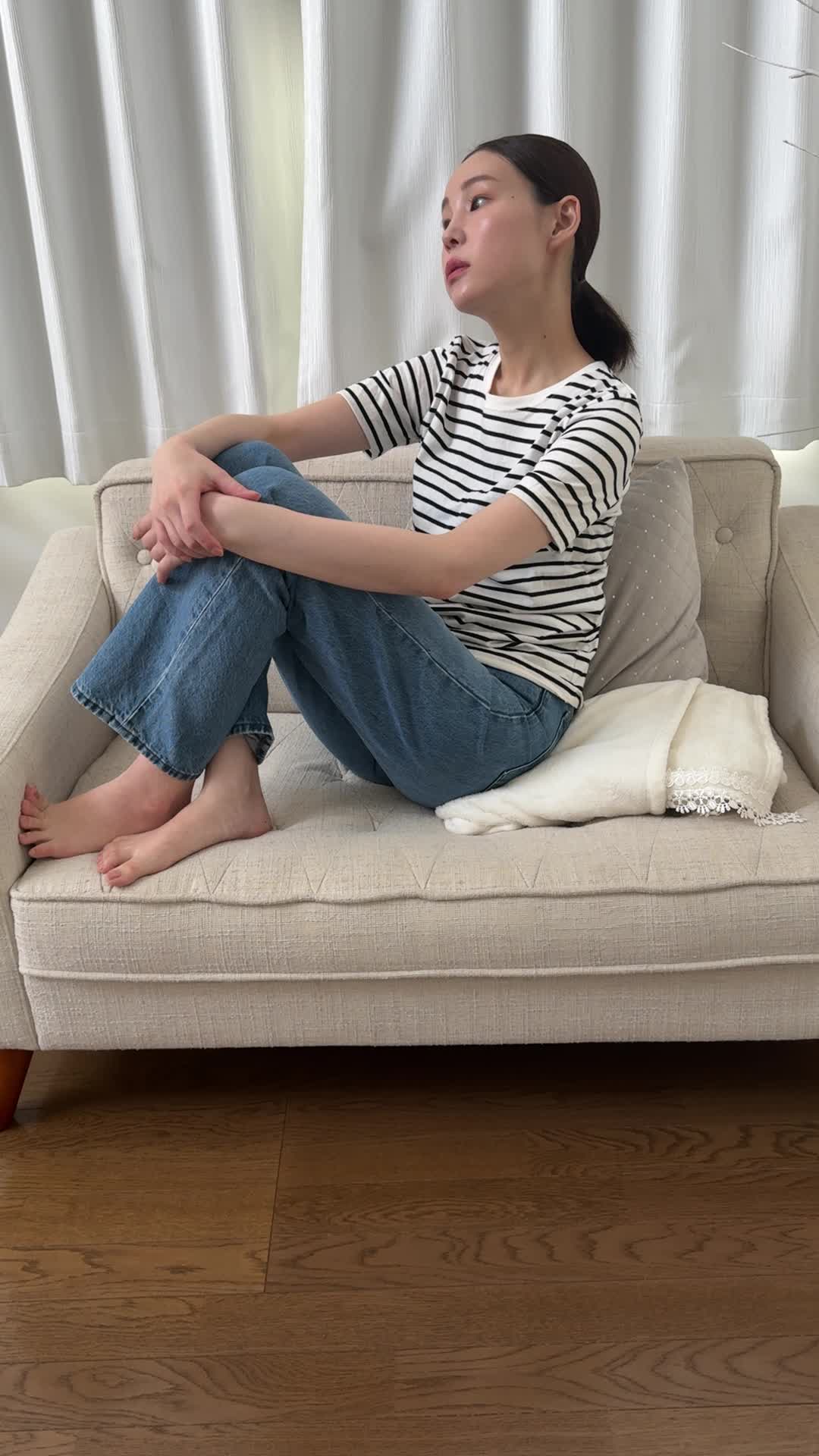 ソファで膝を抱え、「疲れやすくて何もする気が起きない」とため息をつく様子