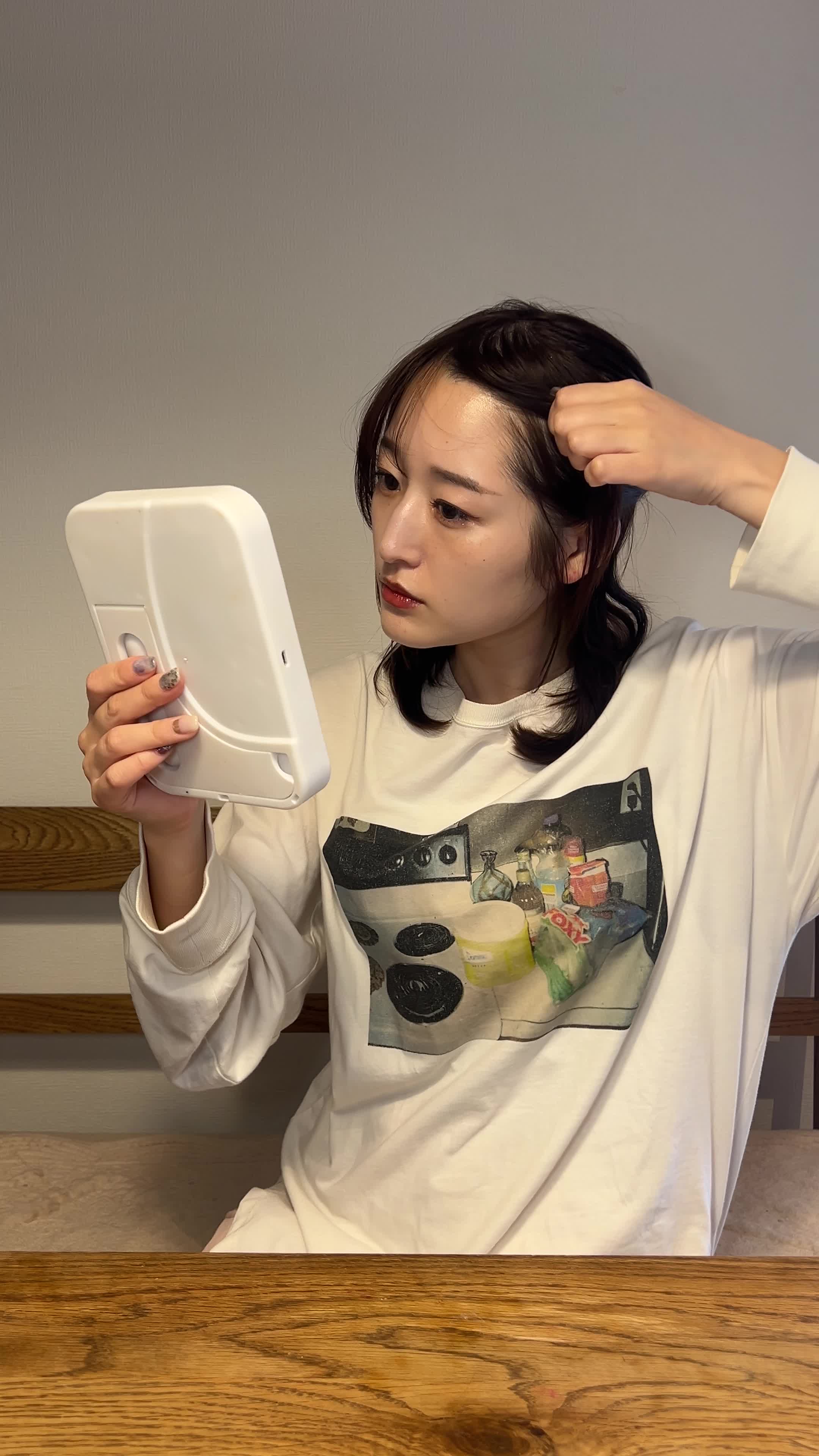 鏡の前で軽く髪をかき上げながらおでこを確認している動作