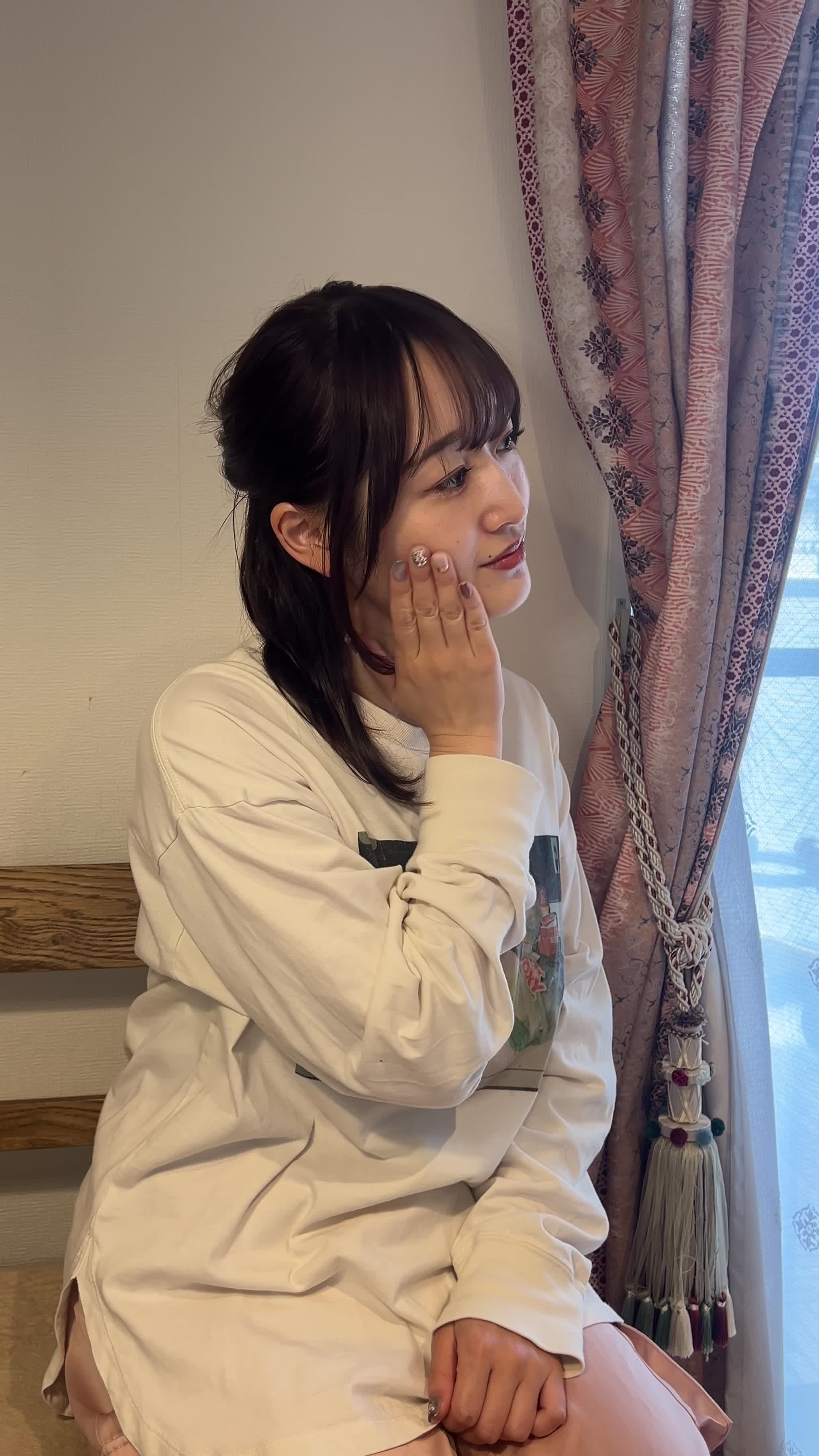 窓際で自然光を浴びながら顔を横に向けて肌を確認する