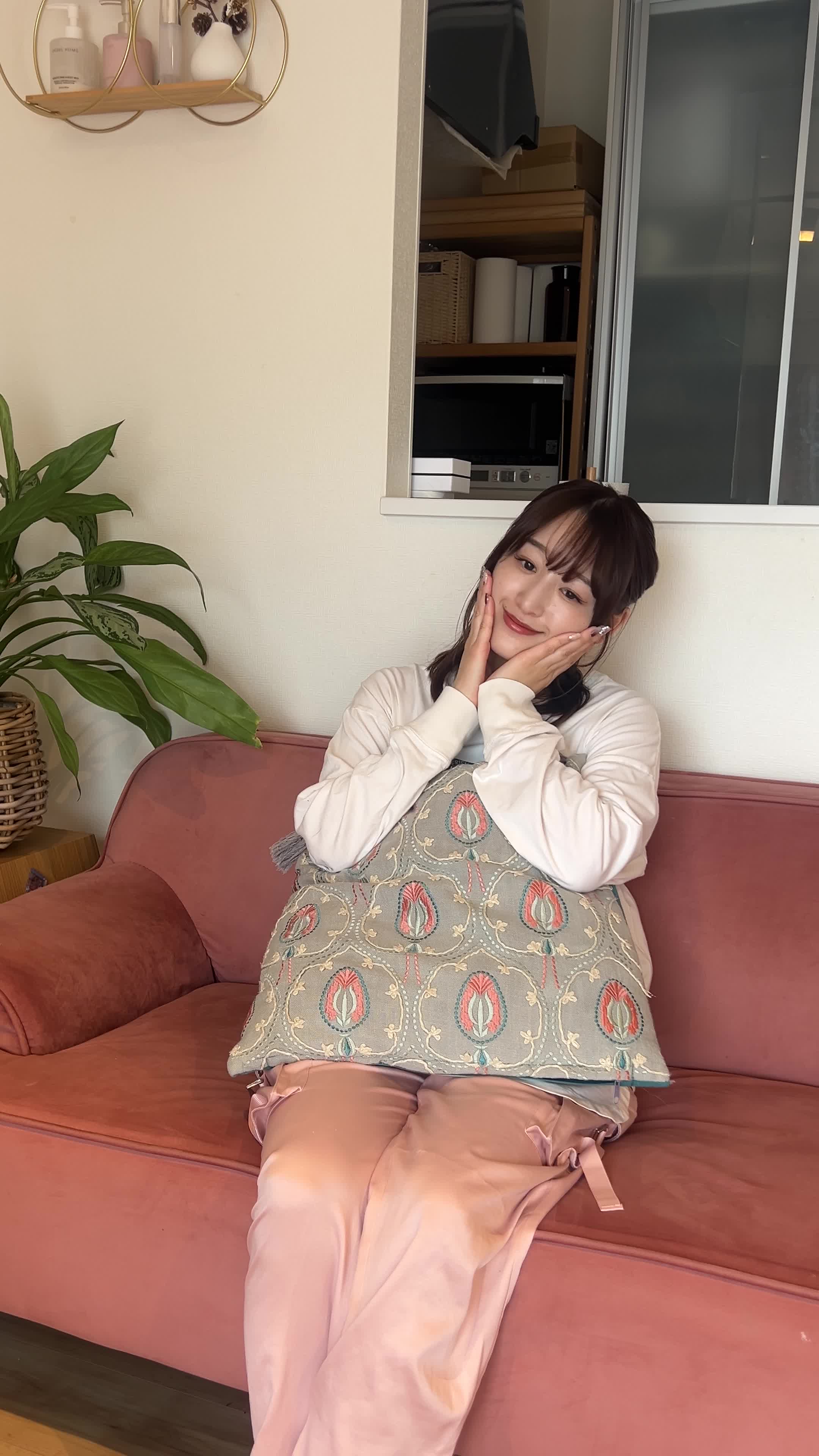 ソファに腰掛け、リラックスしながら両手を頬に当てる仕草をする